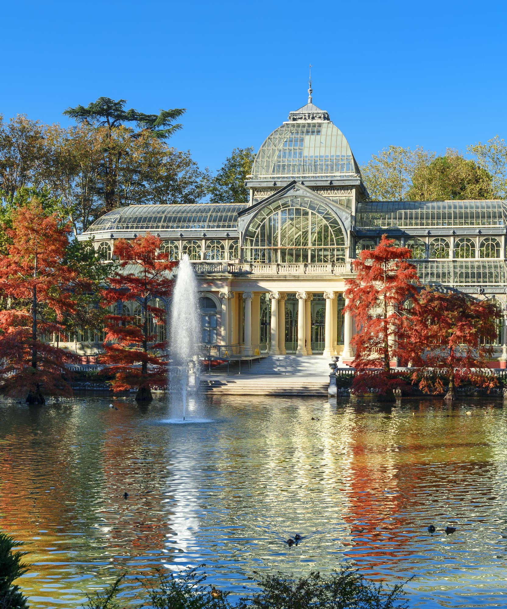Madrid's Crystal Palace in Retiro Park, autumn foliage by the lake.