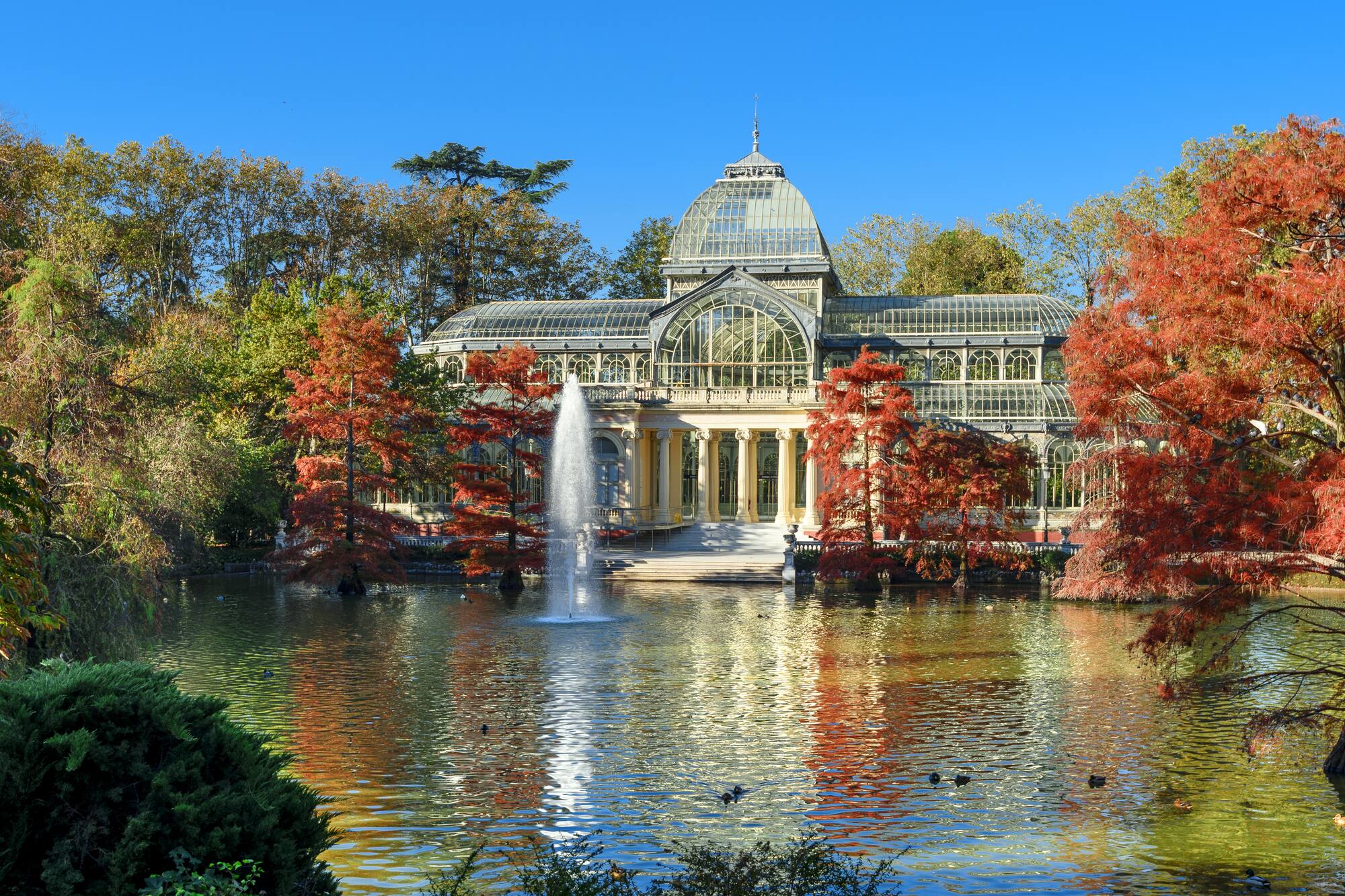 Madrid's Crystal Palace in Retiro Park, autumn foliage by the lake.
