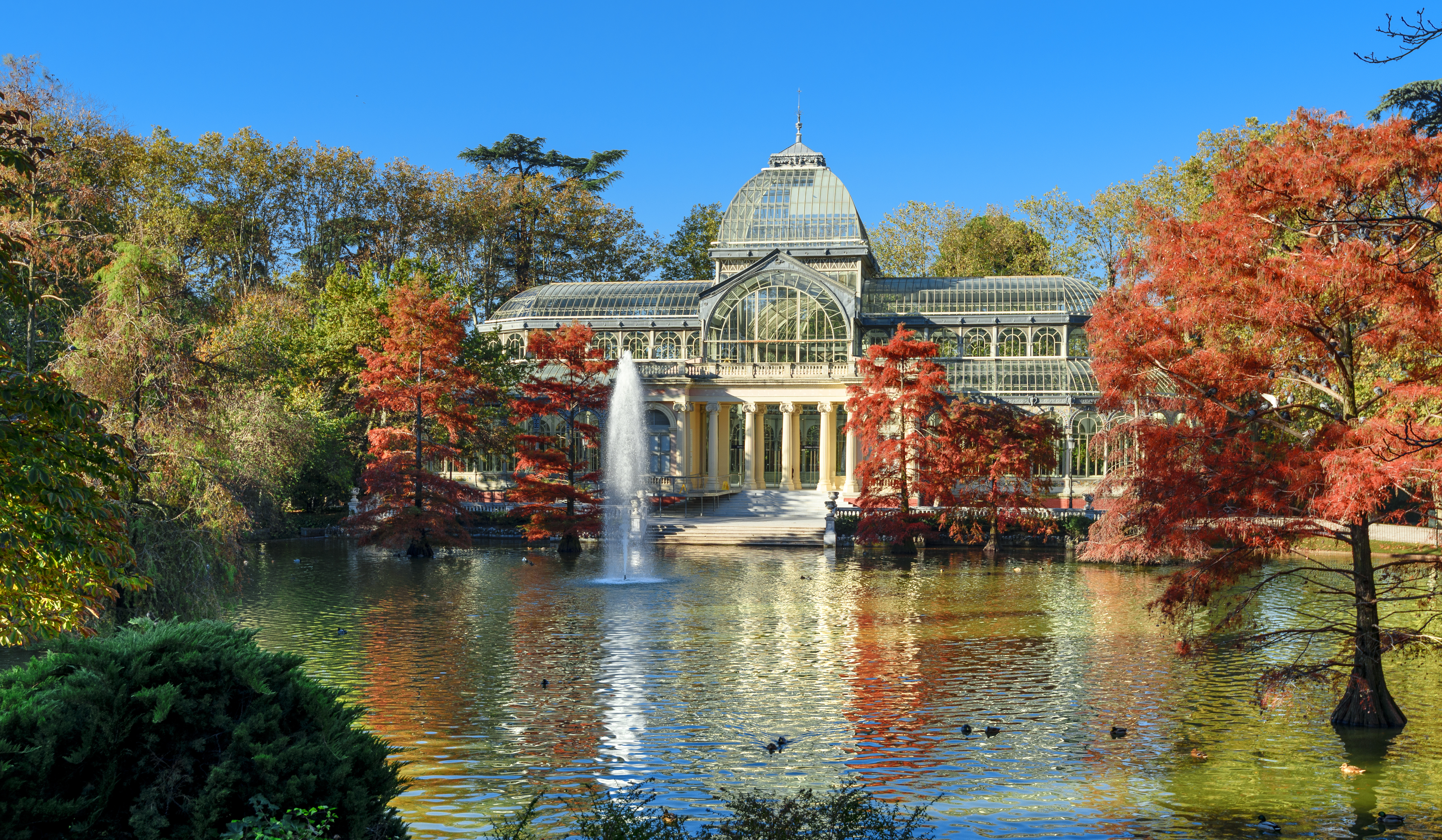 Madrid's Crystal Palace in Retiro Park, autumn foliage by the lake.