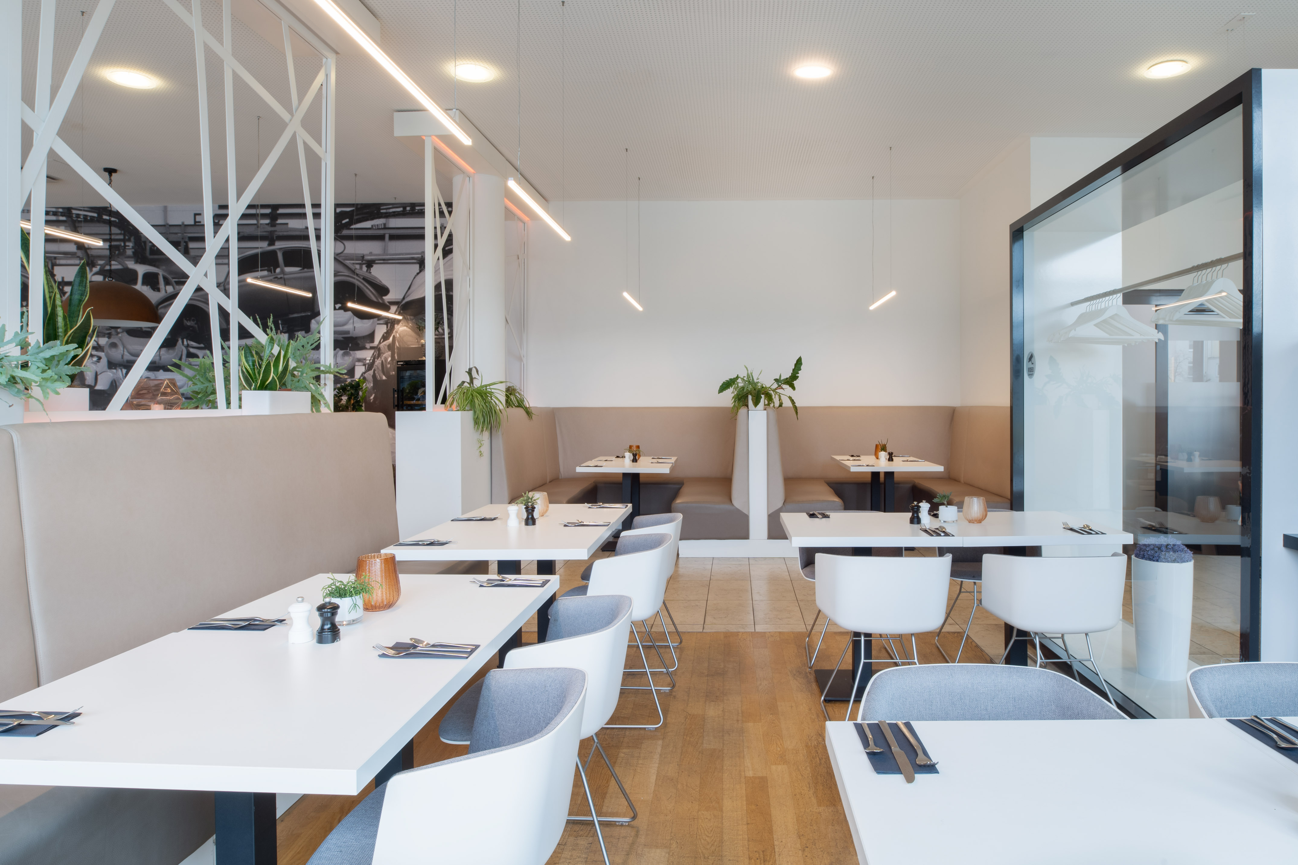 Modern restaurant interior with white tables, booth seating, plants, and wood floor. - Restaurante VEN, Cocina internacional - INNSiDE Wolfsburg, Wolfsburg