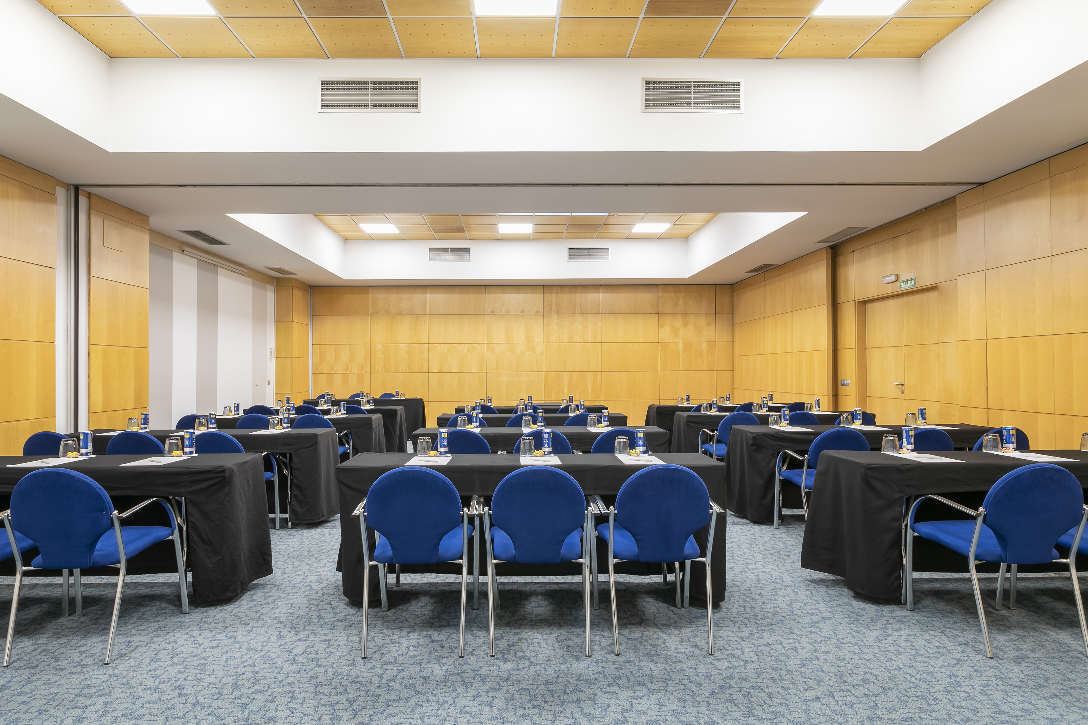 Spacious meeting room with blue chairs, black tables, and light wooden walls.