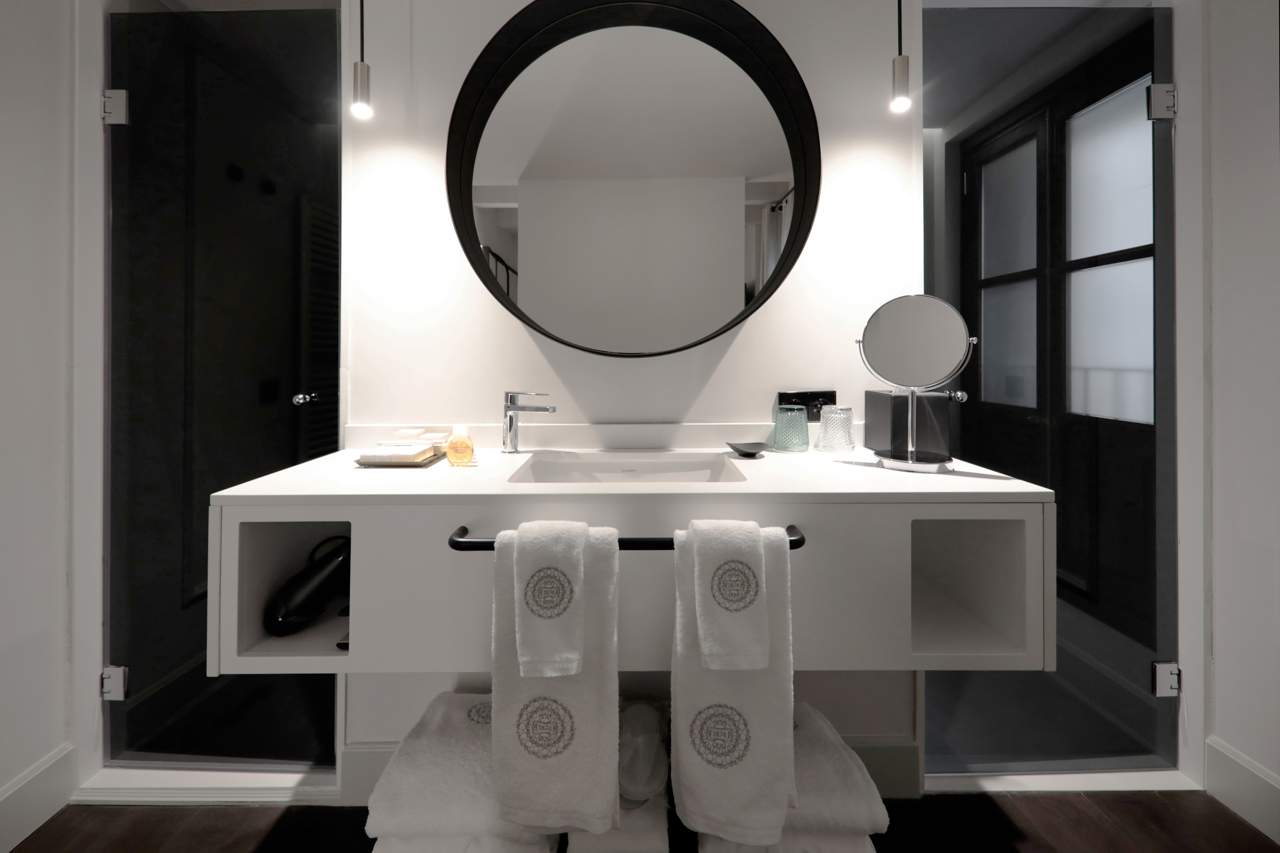Modern hotel bathroom vanity with round mirror, white sink, and clean towels.