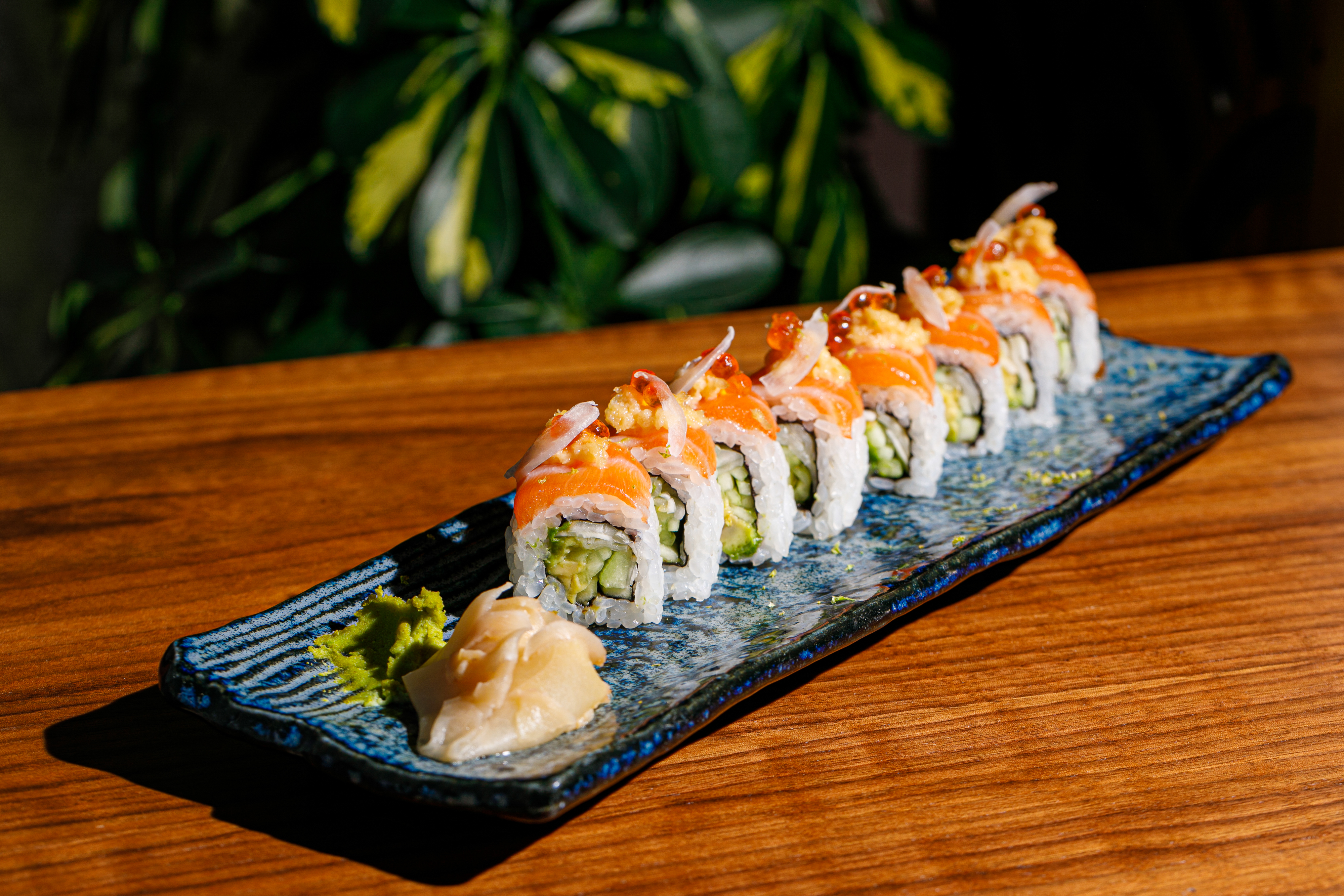 Salmon sushi rolls with crab and roe, wasabi, and ginger on a blue plate.