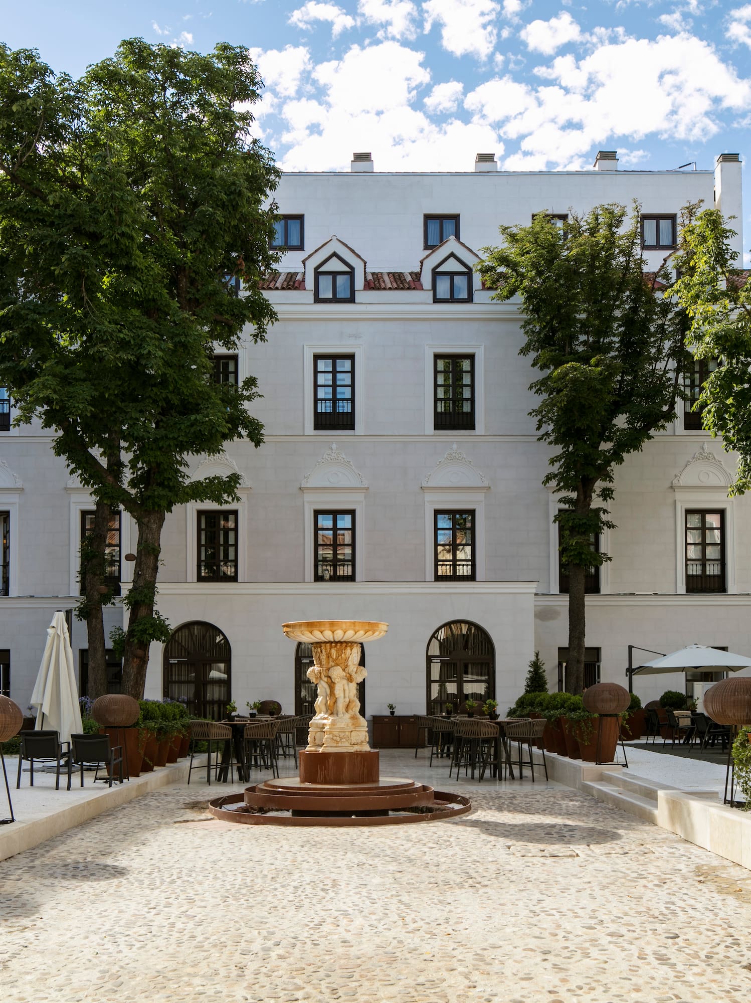 a courtyard with a fountain and trees in front of a building