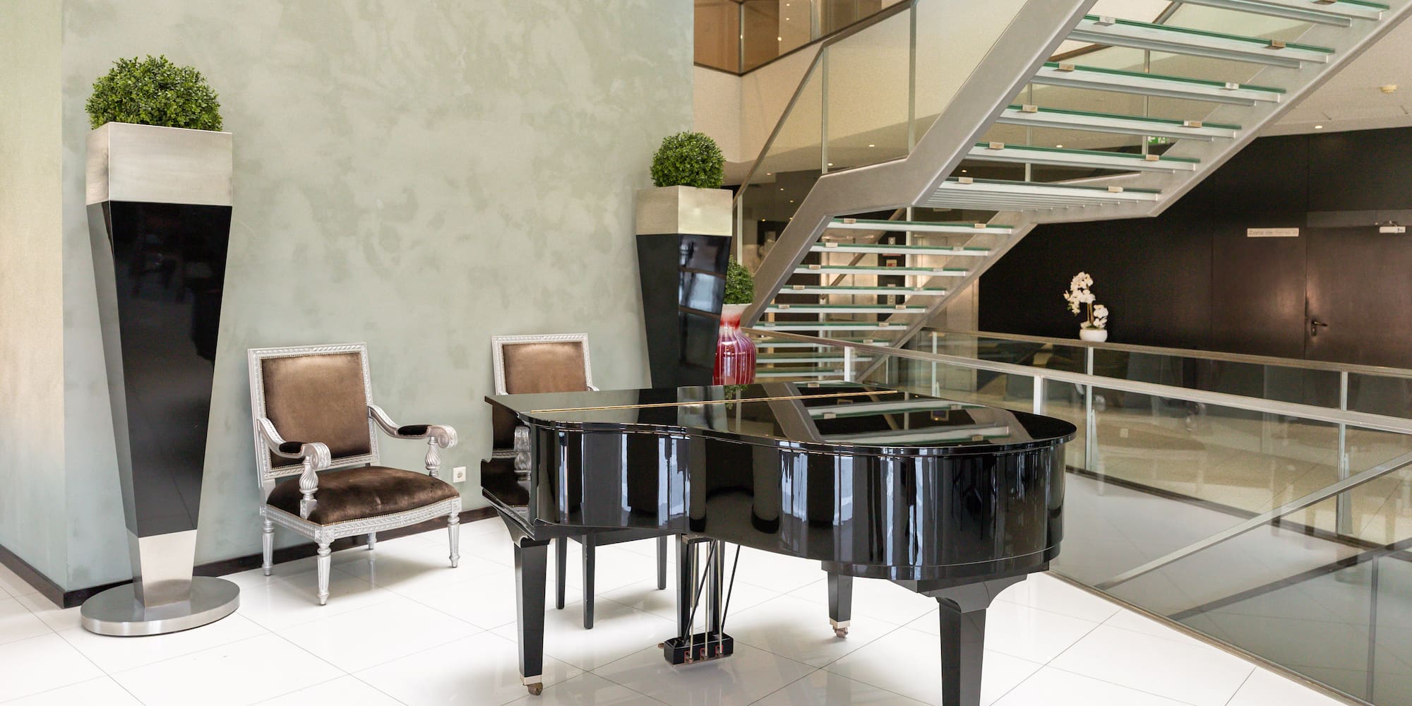 Modern hotel lobby with grand piano, glass staircase, and velvet chairs.