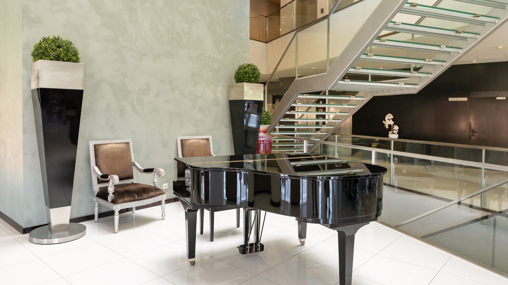 Grand piano in contemporary hotel lobby with sleek glass staircase and elegant chairs.