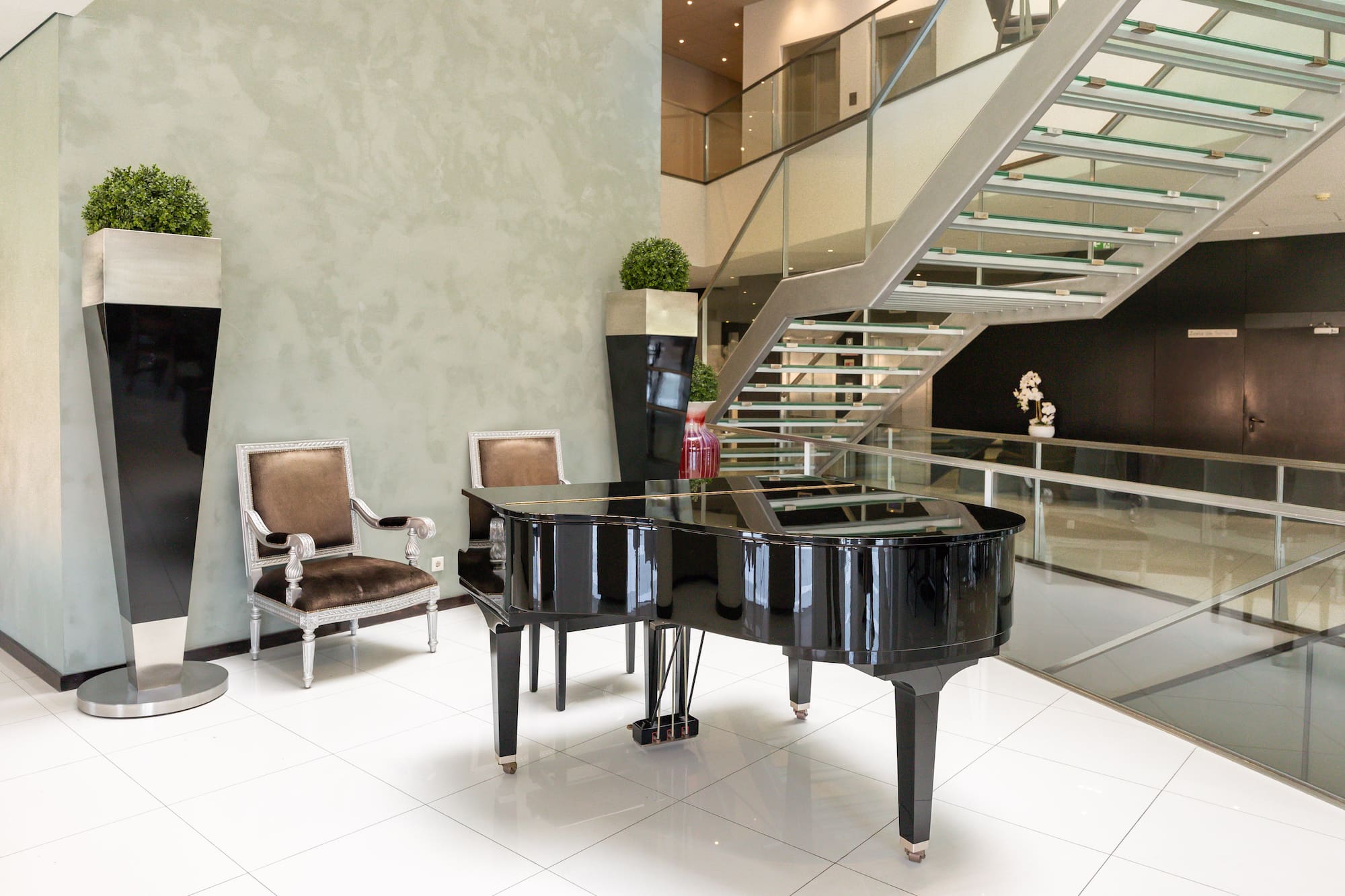 Modern hotel lobby with grand piano, glass staircase, and velvet chairs.