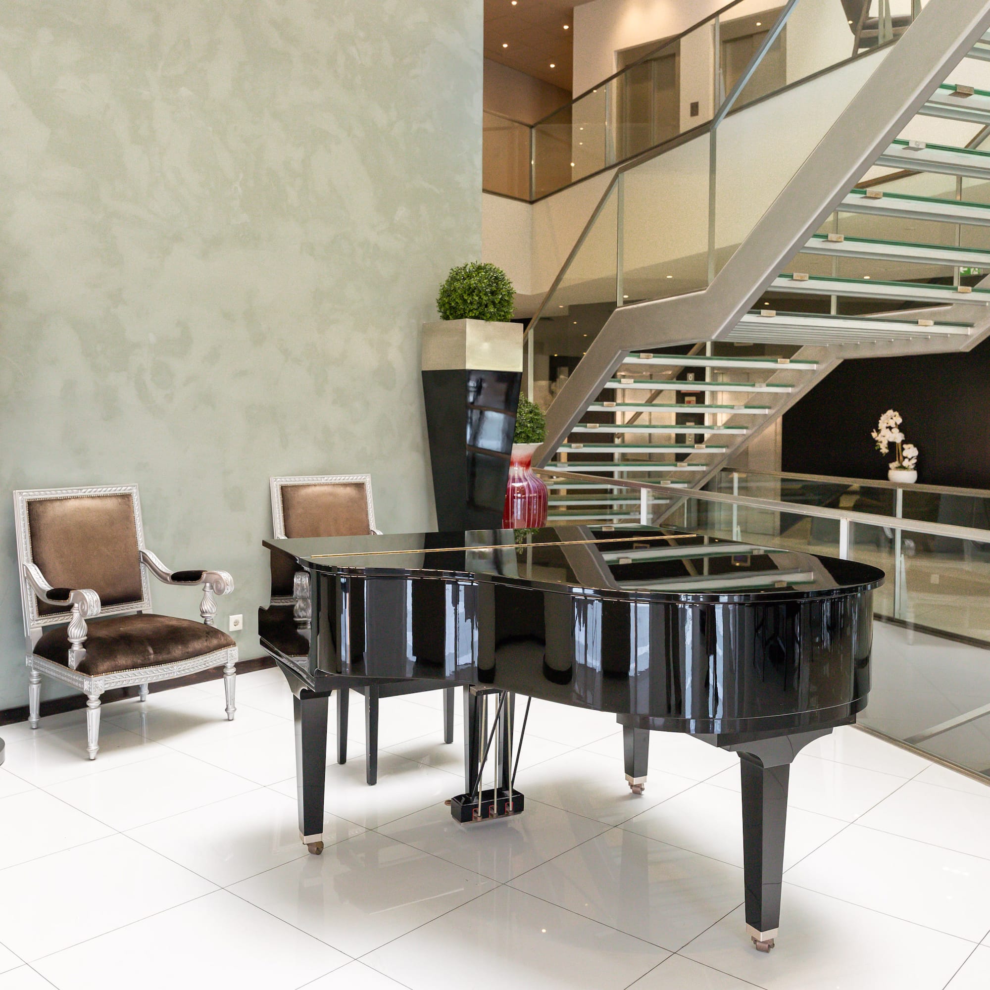 Grand piano in contemporary hotel lobby with sleek glass staircase and elegant chairs.
