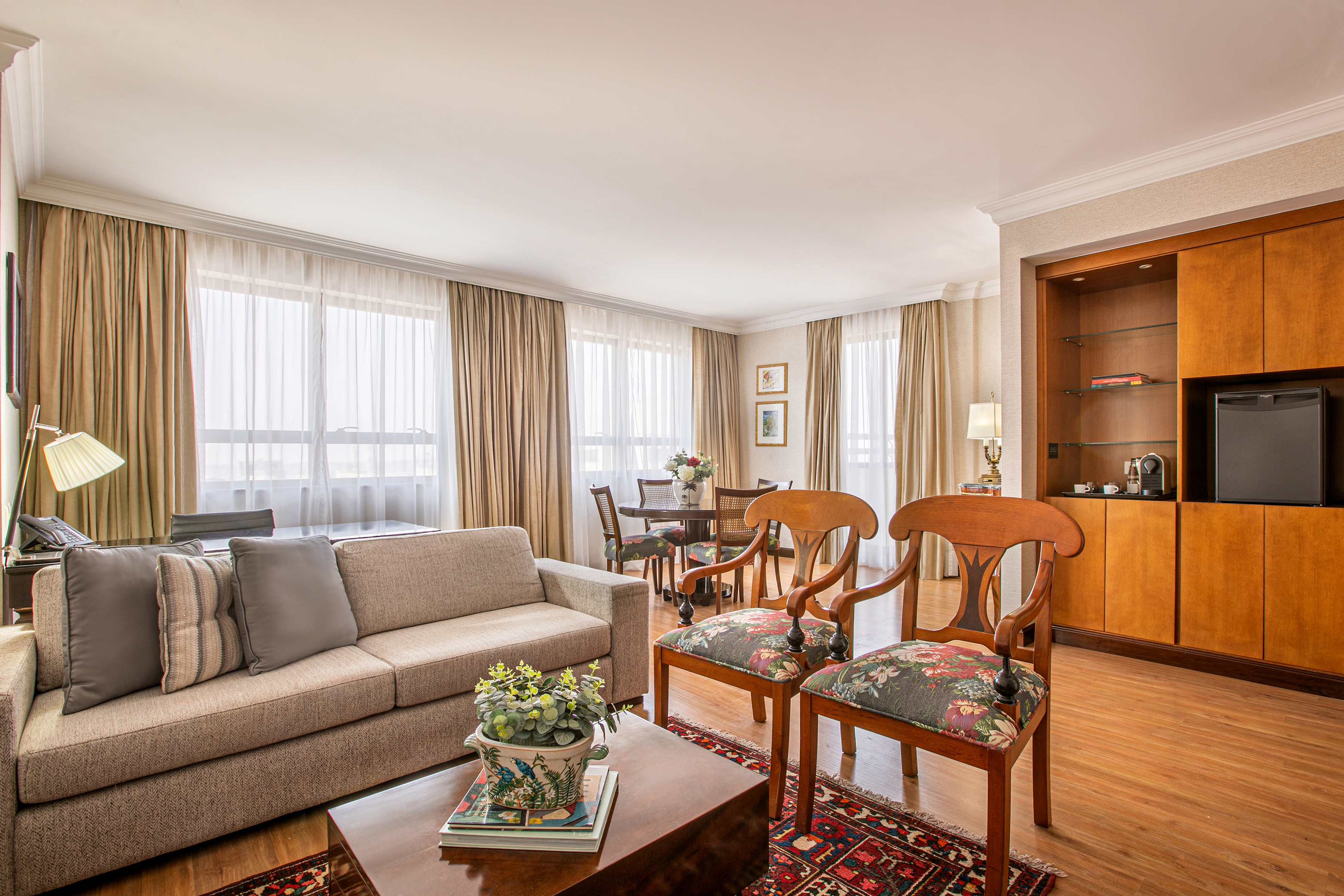 Spacious hotel suite living and dining room with sofa, chairs, and minibar.