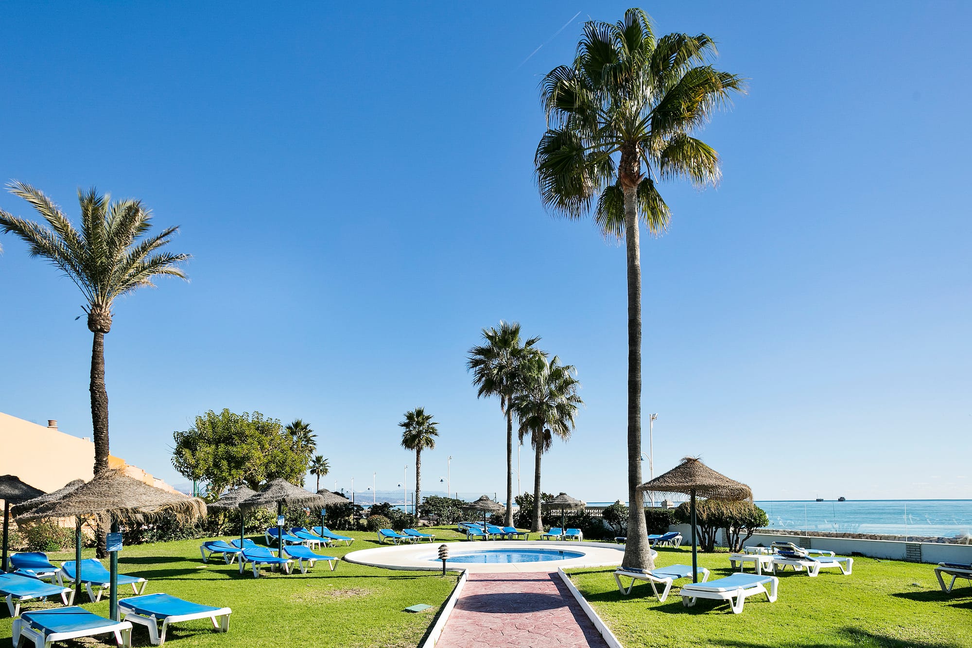 a pool with lounge chairs and umbrellas by a beach