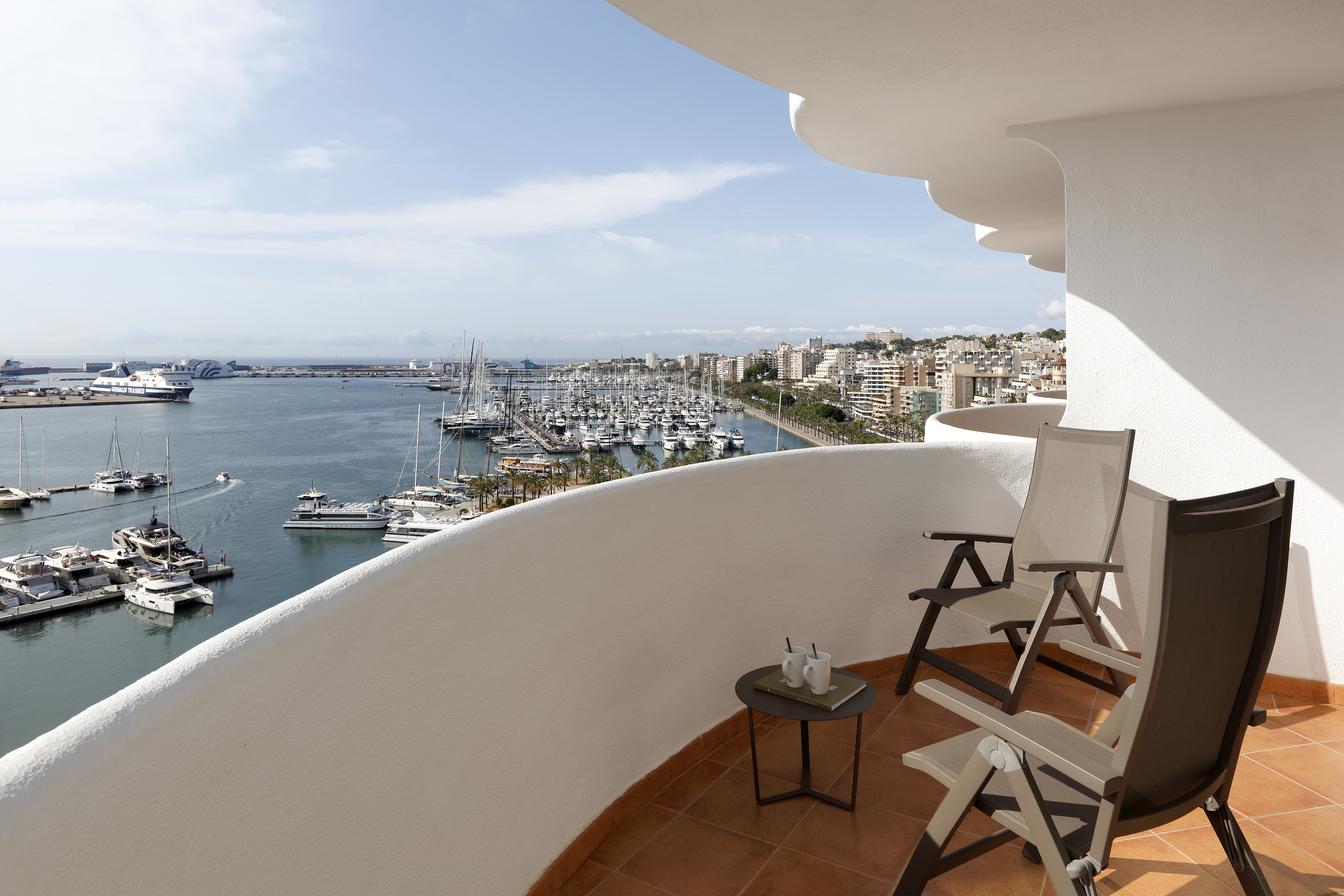 Balcony with chairs, sea view, bustling marina, and coastal city.