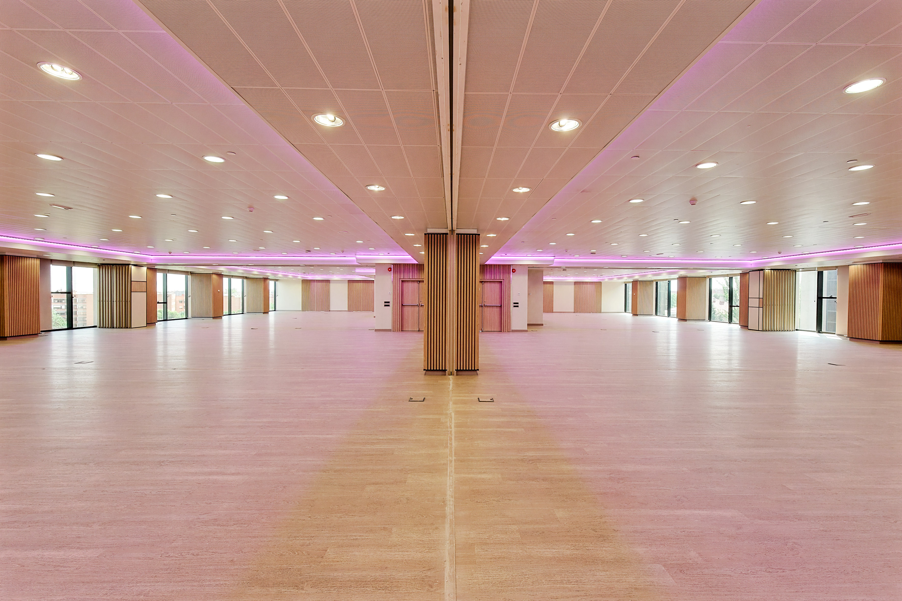 Spacious modern event hall with wood floor, large windows, and pink LED lighting.