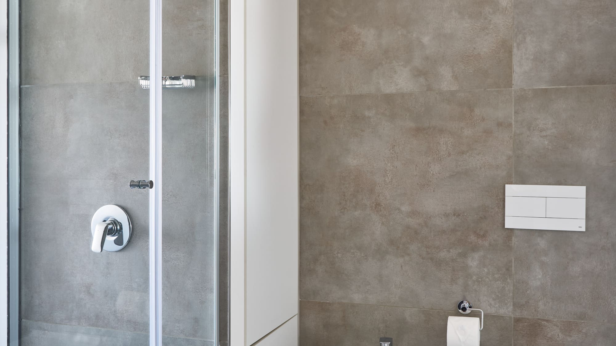Modern bathroom with glass shower, grey tiles, white toilet, and bidet.