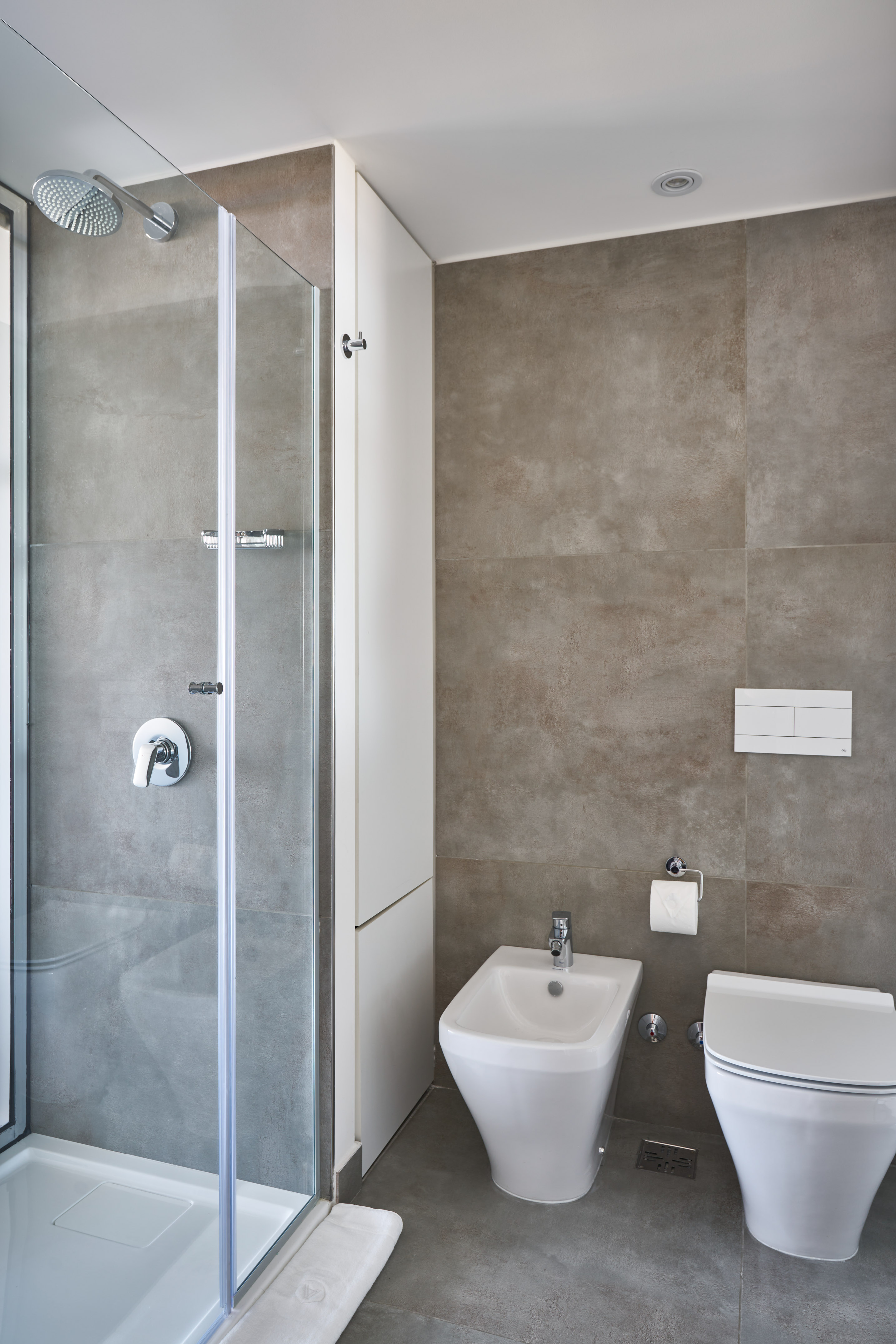 Modern bathroom with glass shower, grey tiles, white toilet, and bidet.