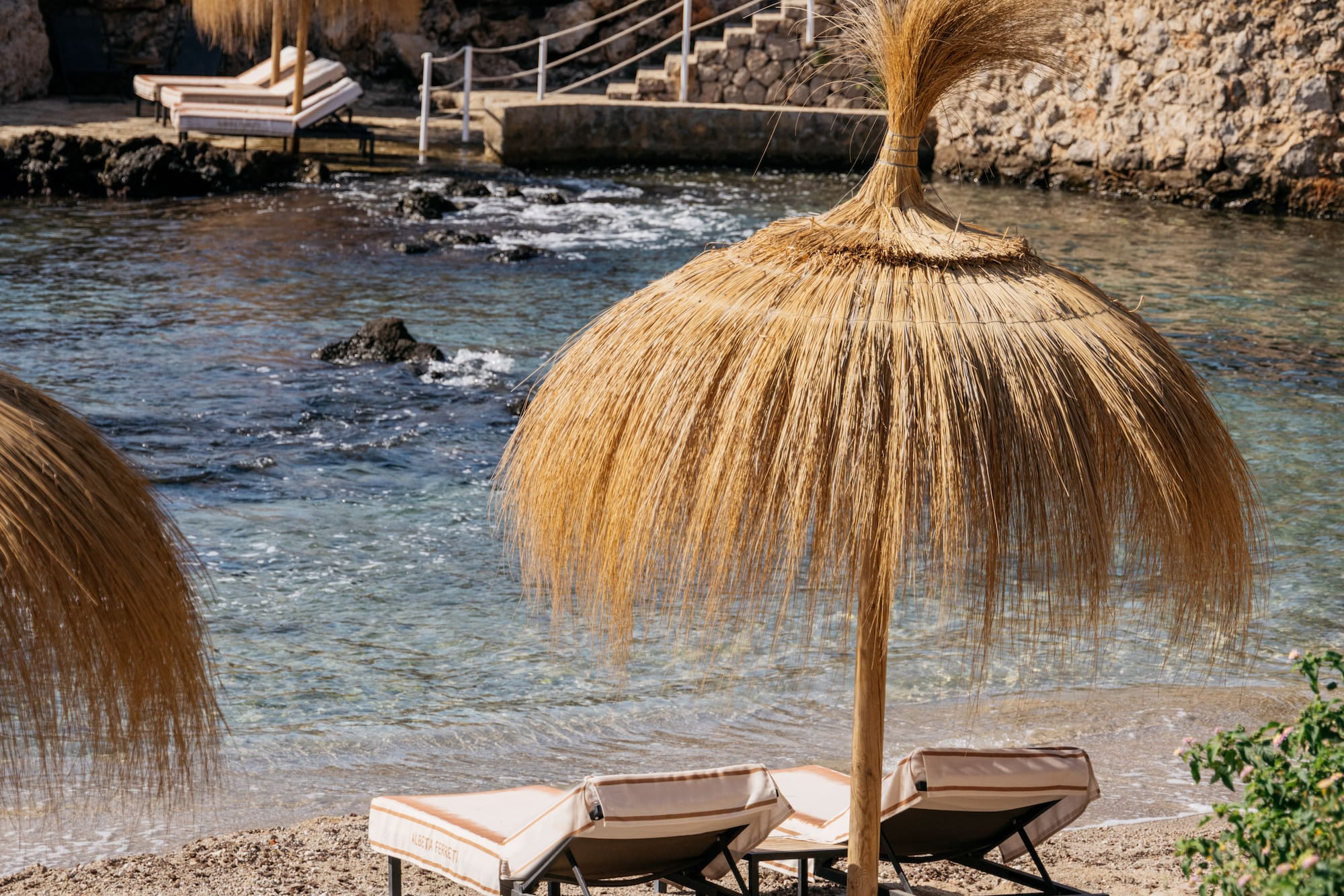 Luxury beach resort with straw umbrellas, sunbeds, clear sea, rocky cliffs.