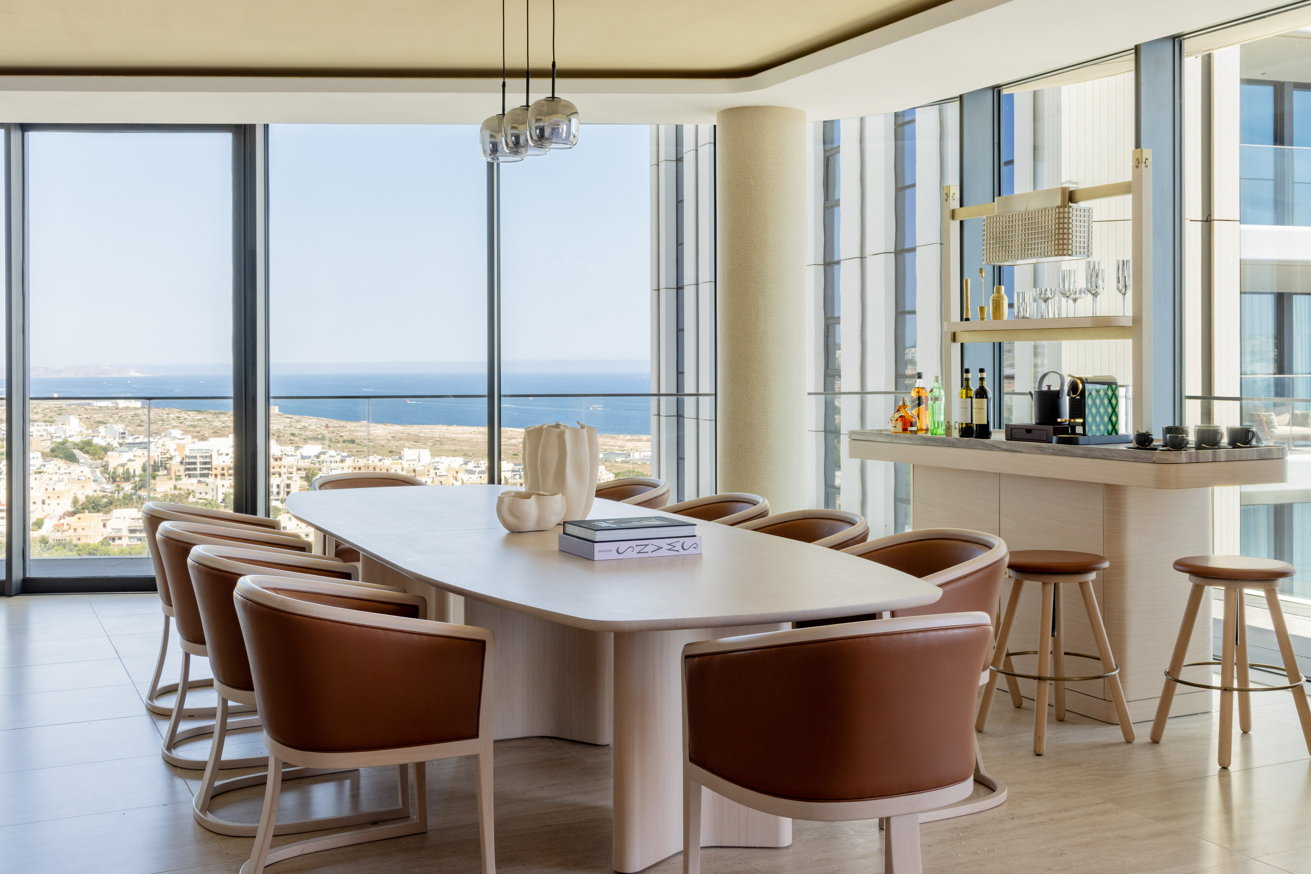 Modern dining room with sea view, long wooden table, leather chairs, and bar area.