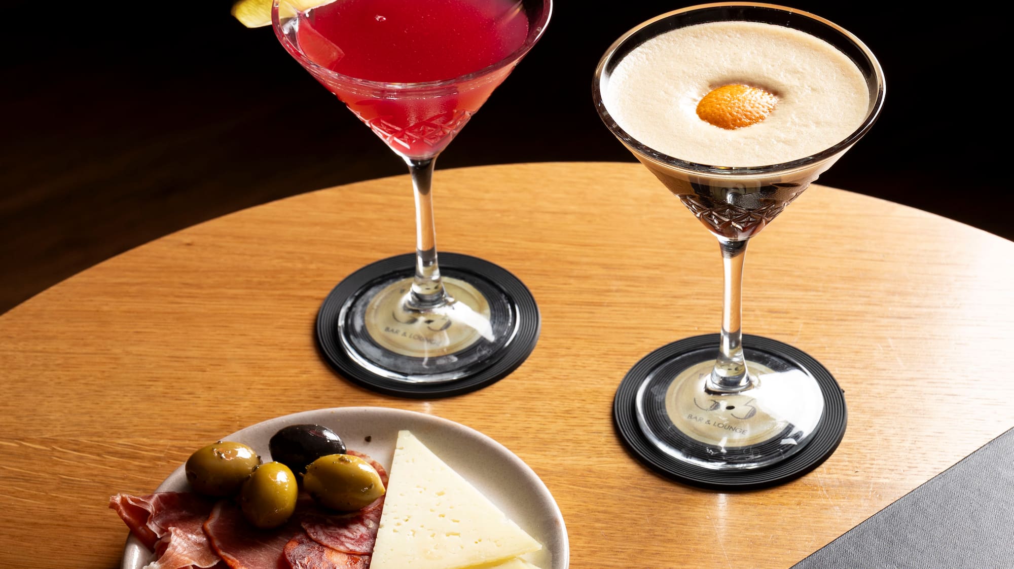 Martini cocktails, charcuterie board, and lounge menu on wooden table.