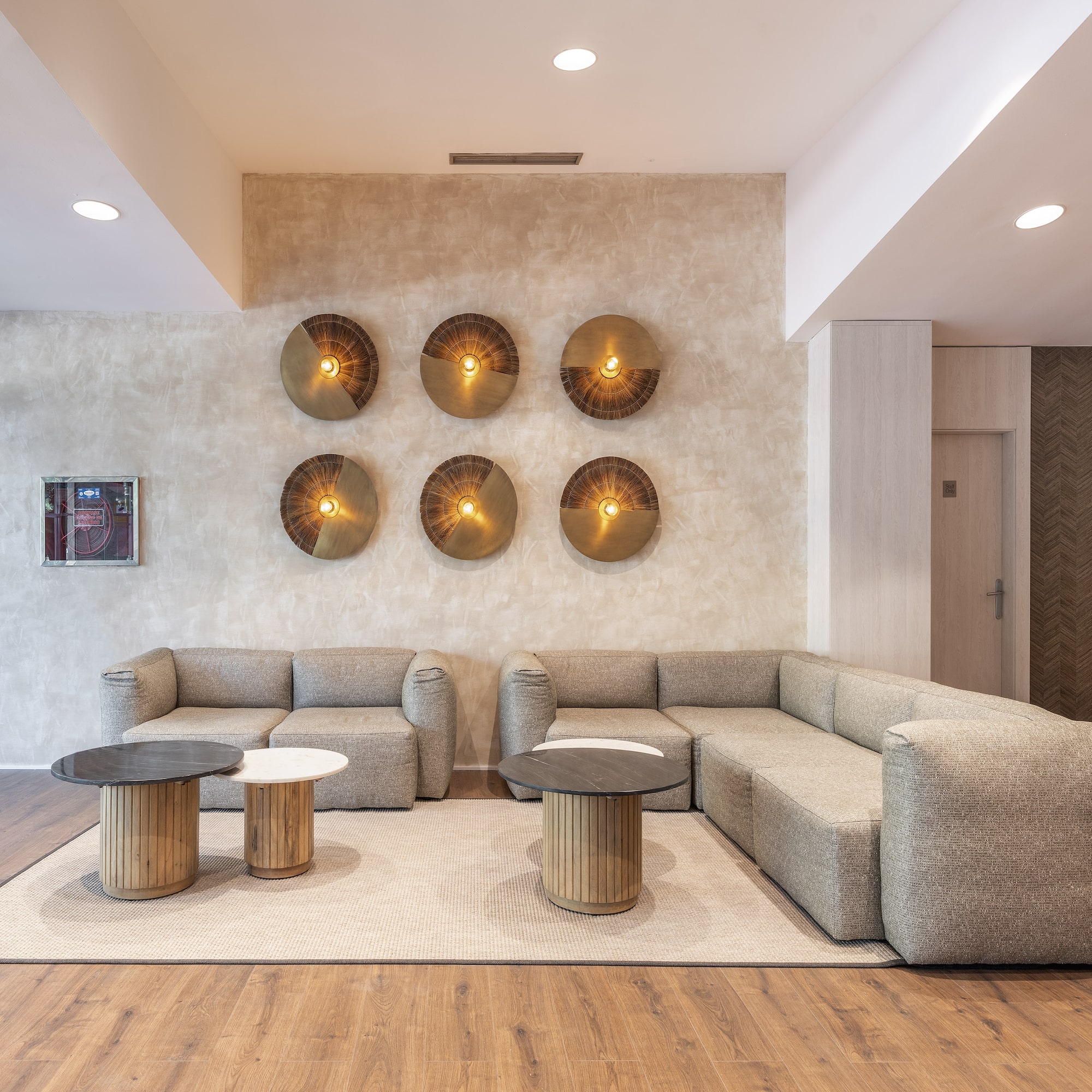 Modern hotel lounge with neutral sofas, wooden tables, and decorative wall lights.