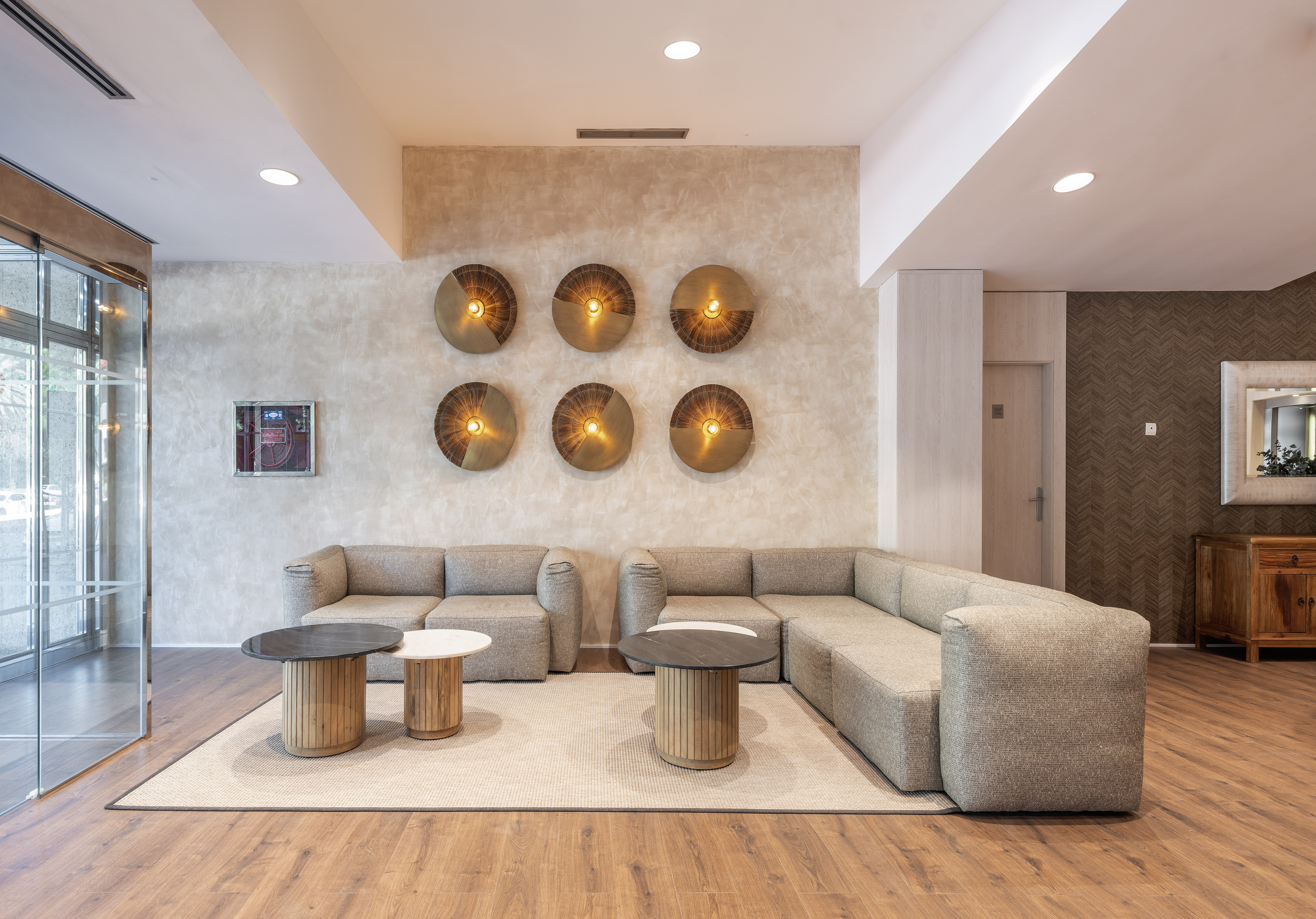 Modern hotel lounge with neutral sofas, wooden tables, and decorative wall lights.