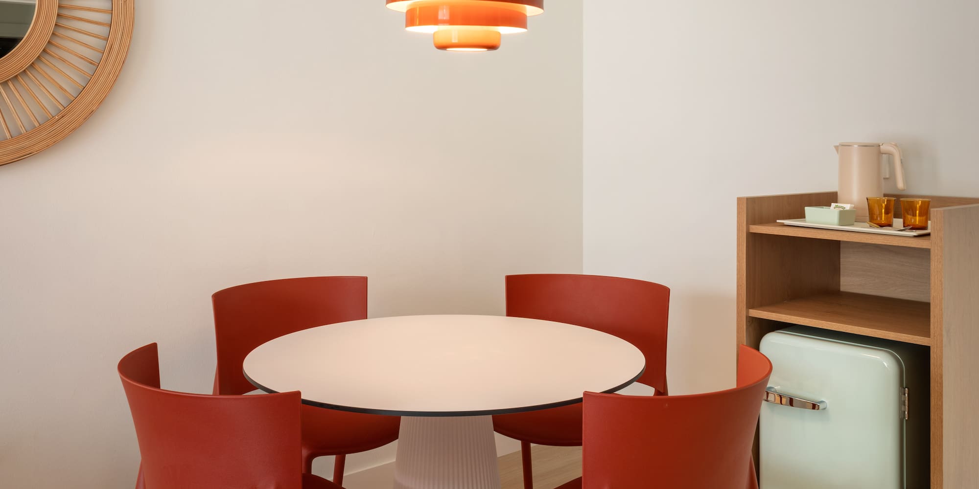 Dining nook: white table, orange chairs, tiered light, green mini-fridge.