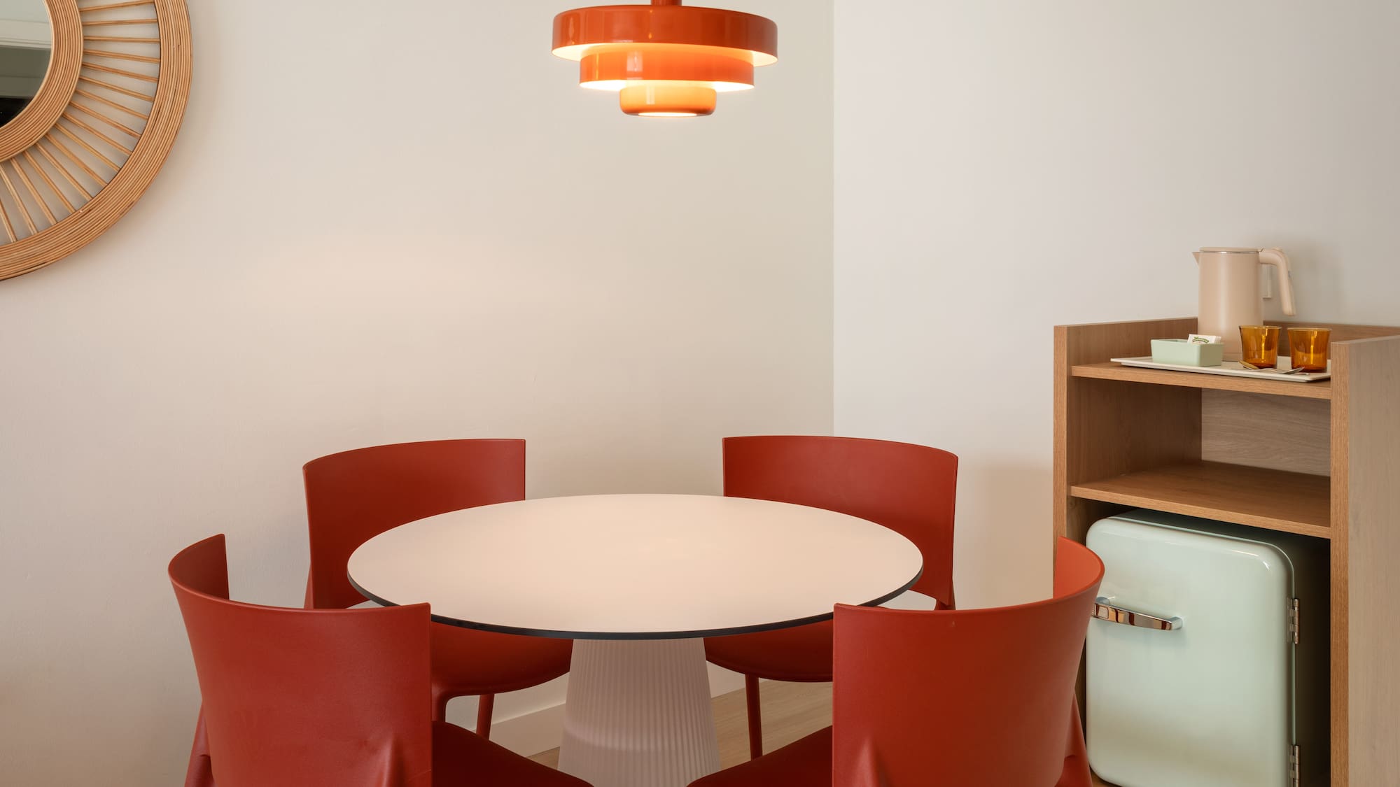 Modern dining area: white table, red chairs, orange pendant, retro mini-fridge.
