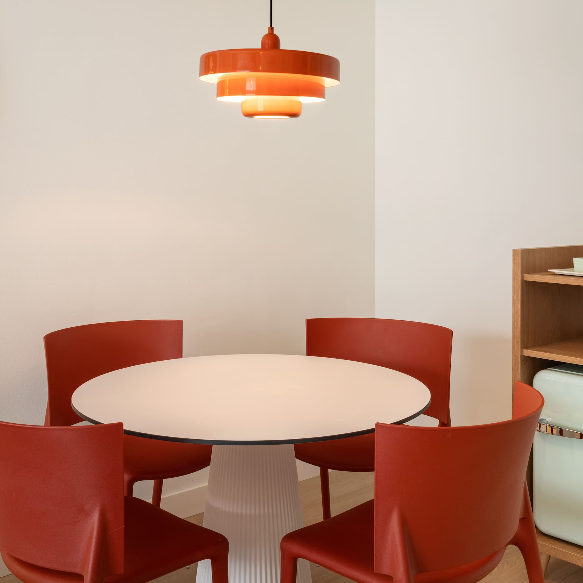 Dining nook: white table, orange chairs, tiered light, green mini-fridge.