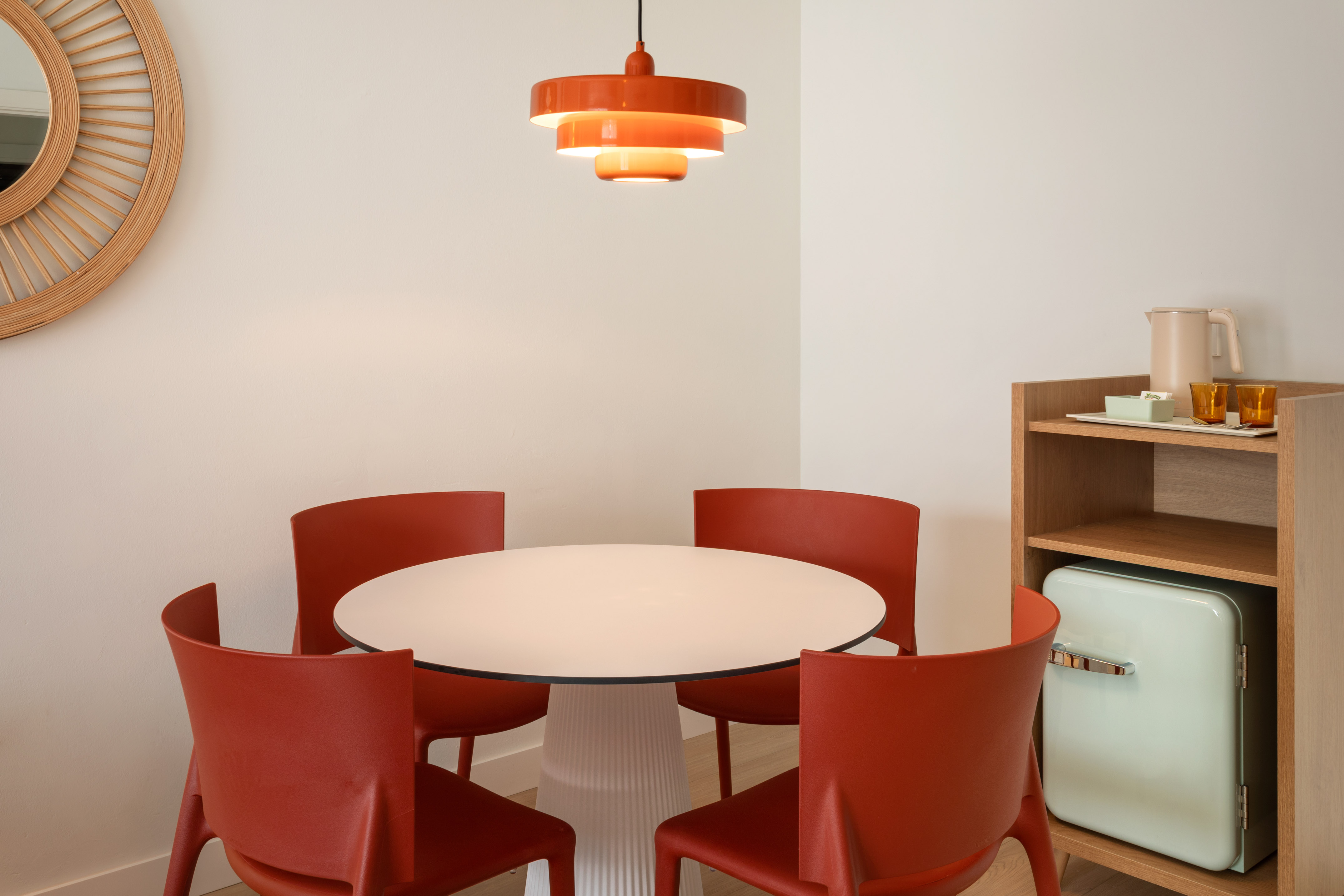 Modern dining area: white table, red chairs, orange pendant, retro mini-fridge.