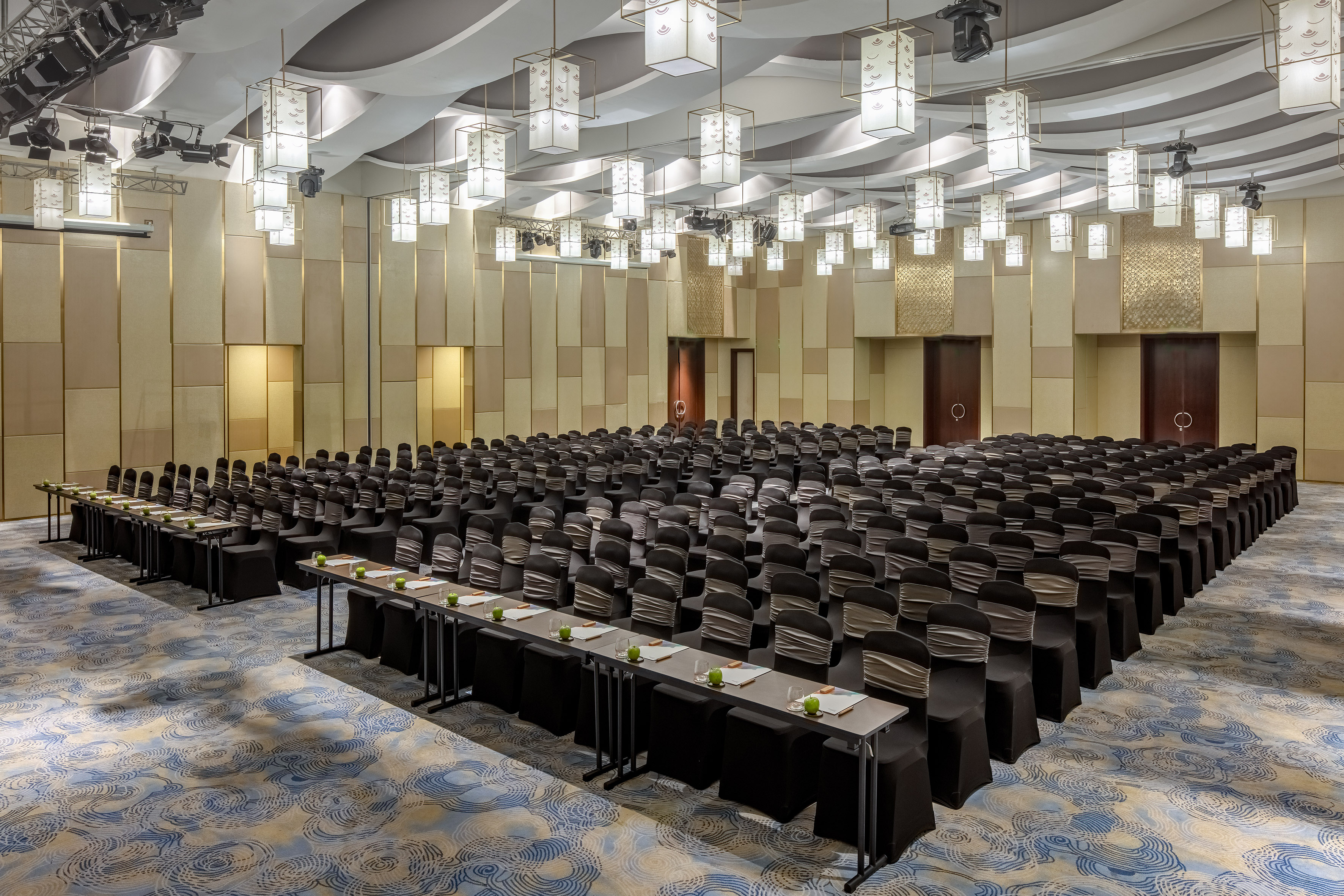 Elegant conference ballroom with chairs, tables, and unique ceiling lighting.