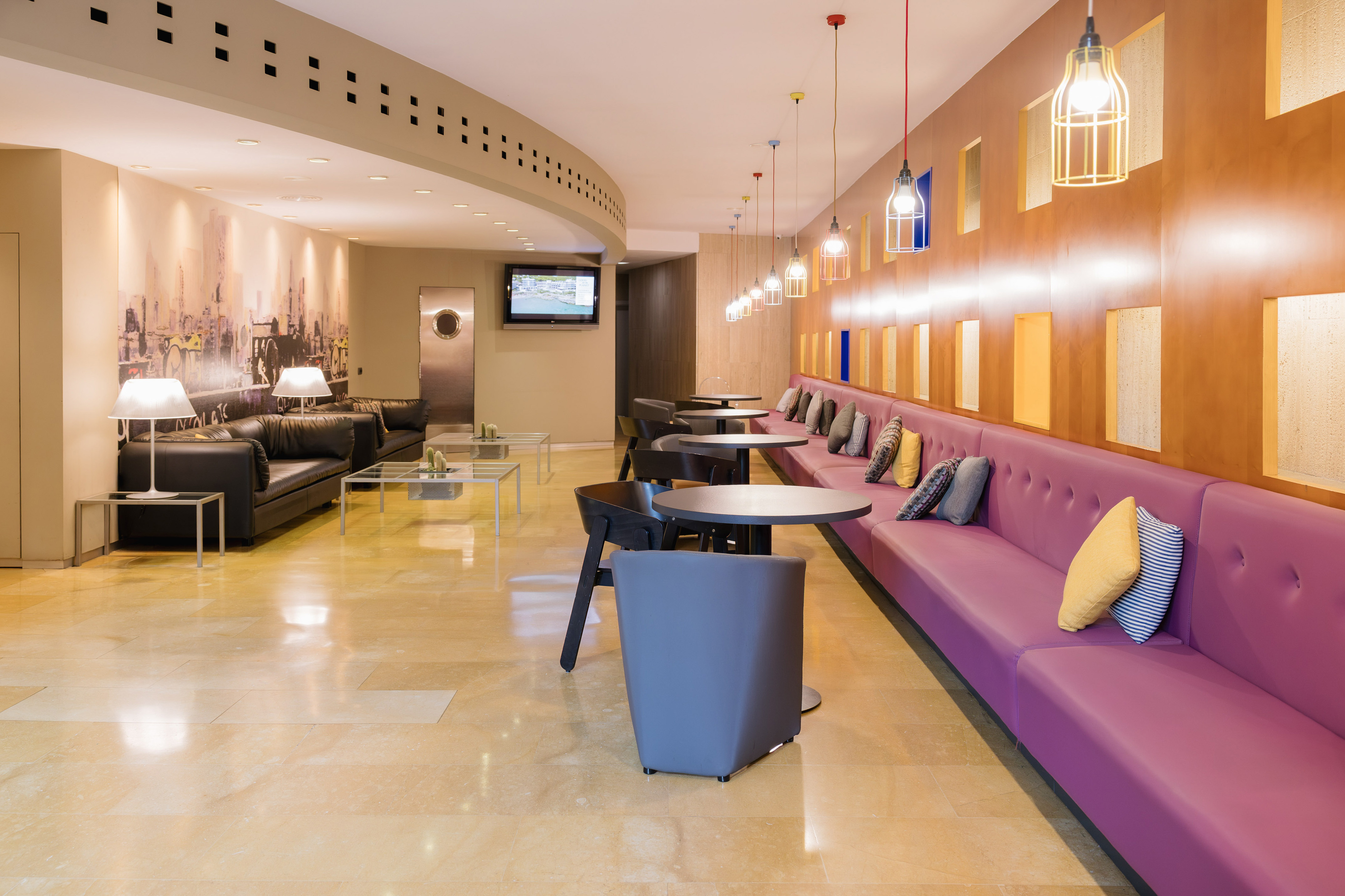 Modern hotel lobby with purple bench seating, black sofas, and pendant lights.