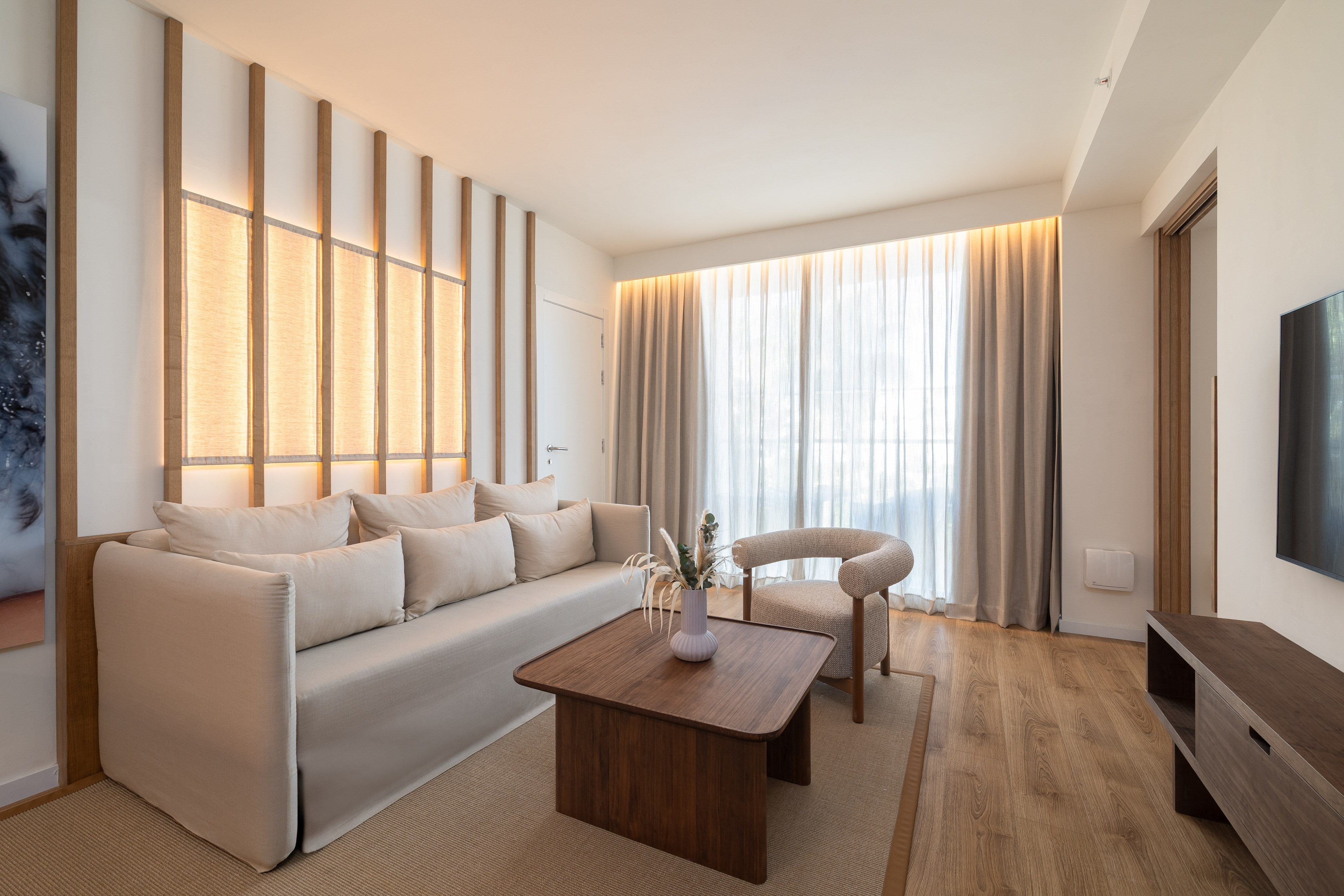 Modern living room with light sofa, wood coffee table, and backlit wall.