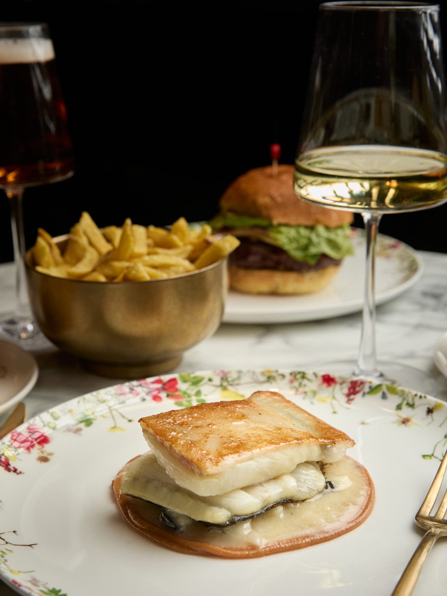 Pan-seared fish with melted cheese, fries, burger, beer, and white wine.