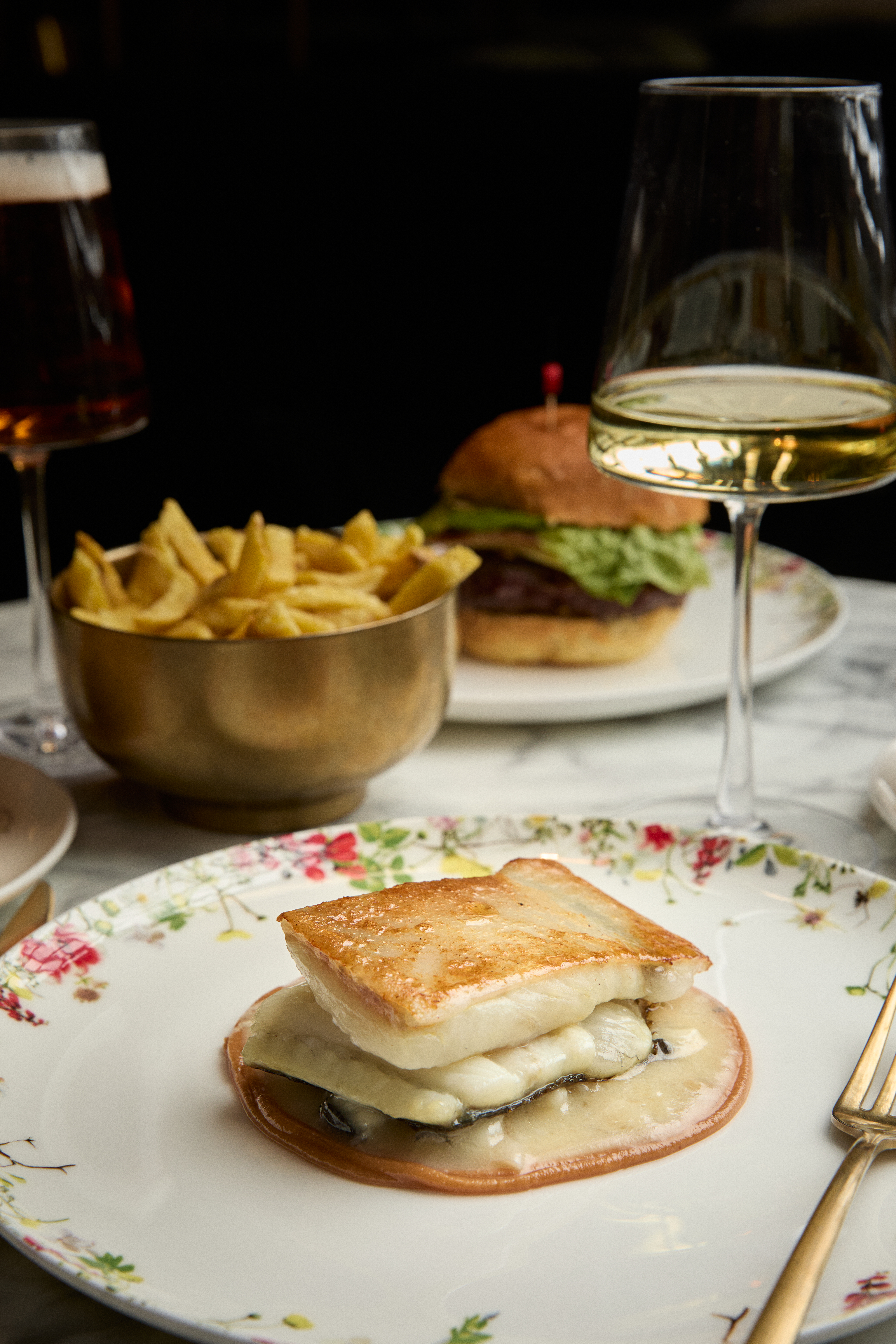 Pan-seared fish with melted cheese, fries, burger, beer, and white wine.