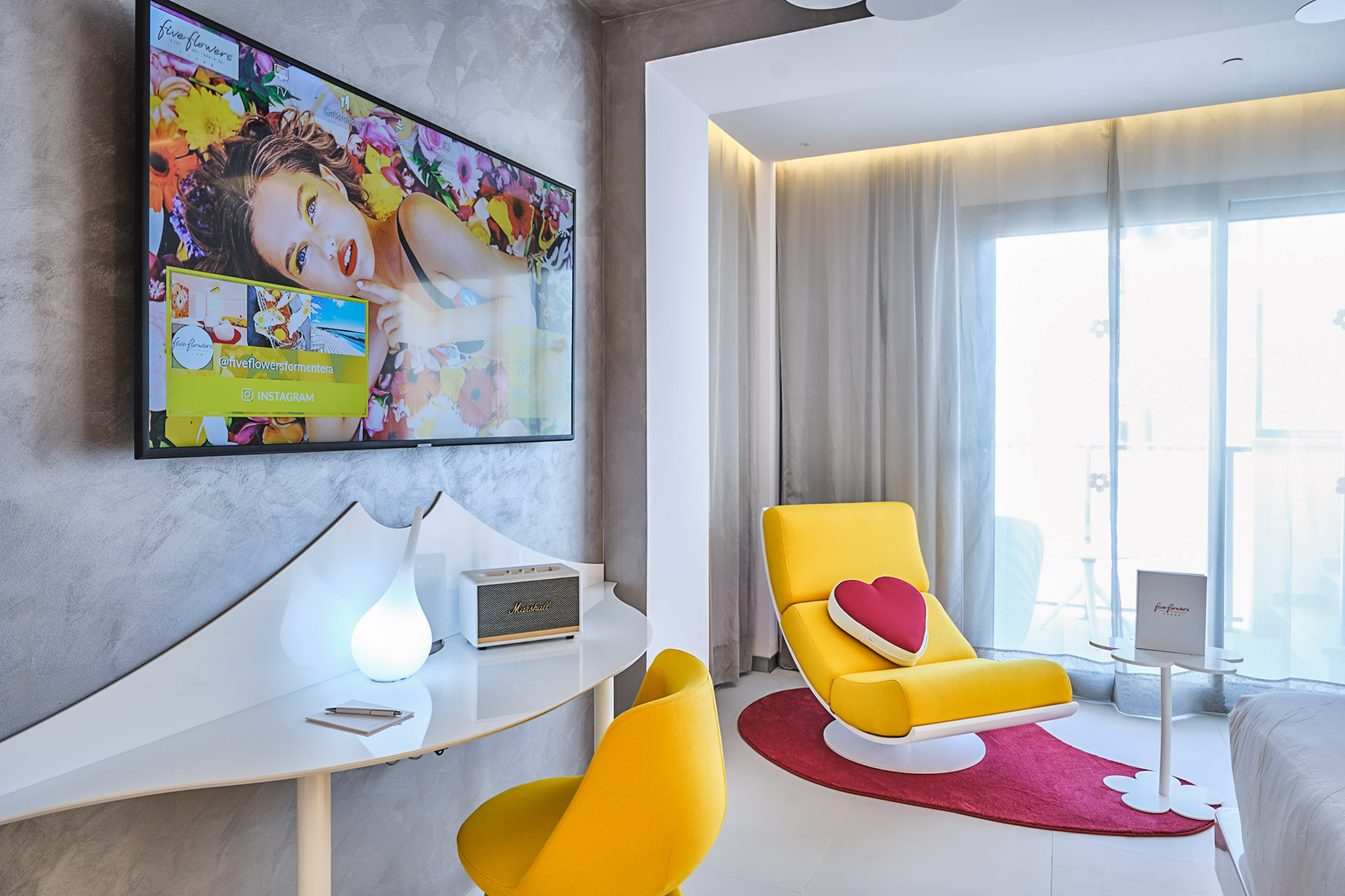 Vibrant modern hotel suite featuring TV, yellow chairs, white desk, and balcony.
