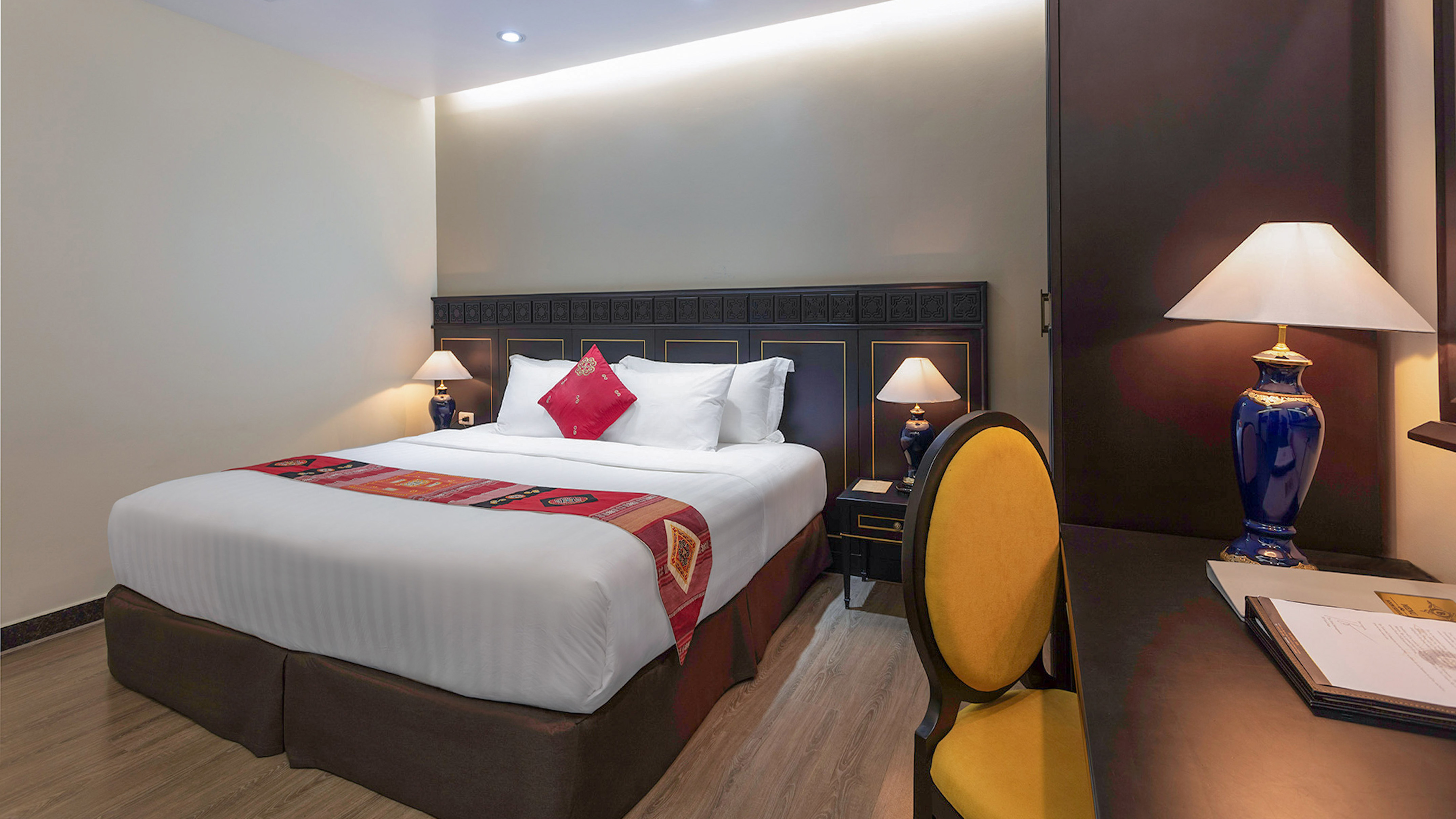 Modern hotel room with comfortable bed, ornate dark wood headboard, and bedside lamps.