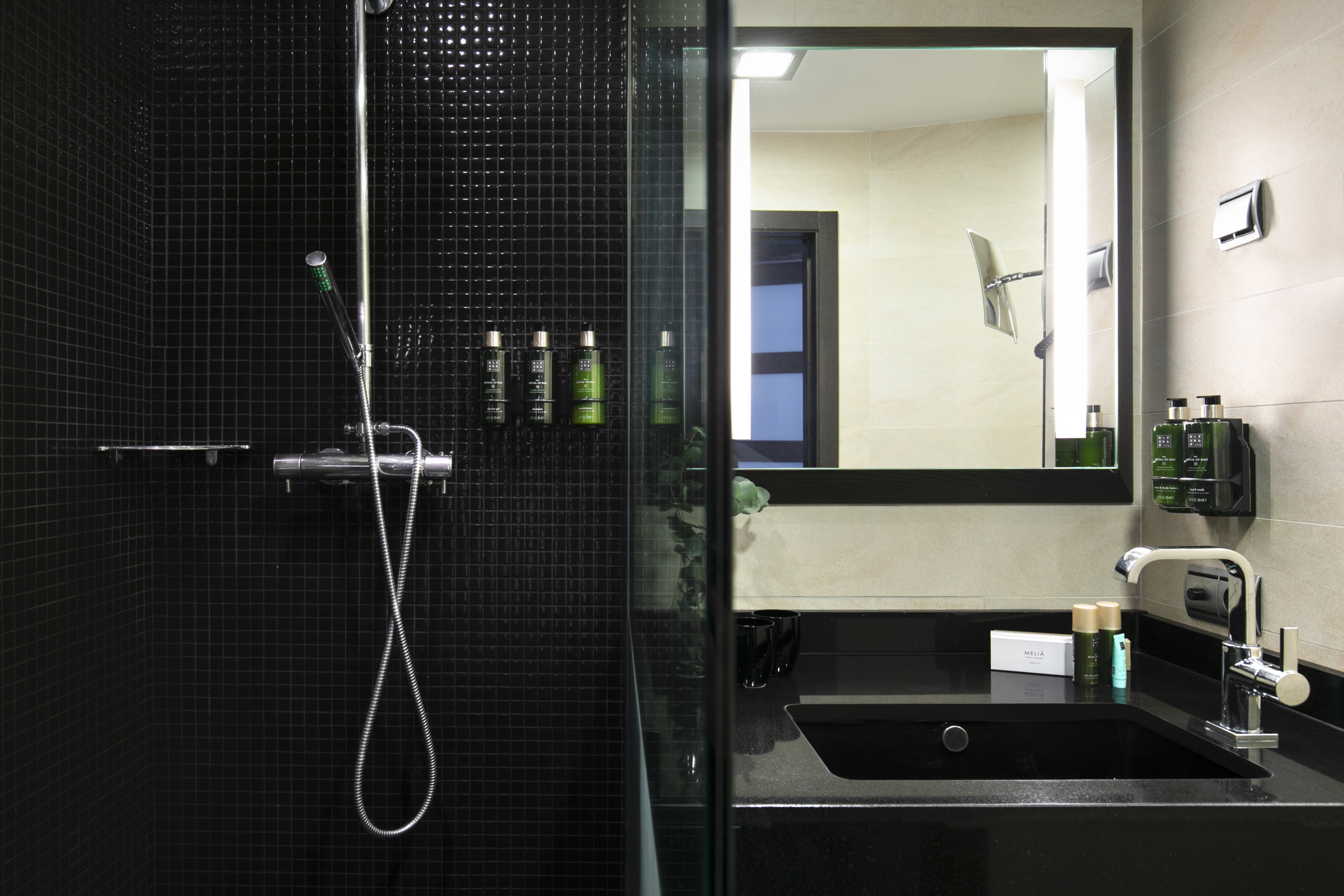 Modern hotel bathroom with black mosaic shower, dark vanity, and amenities.
