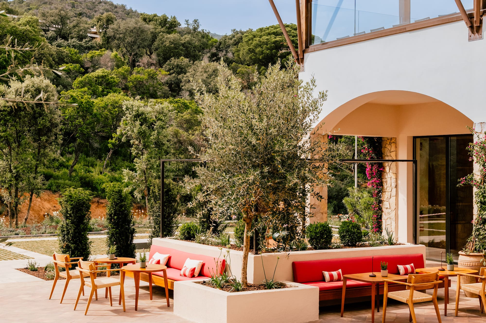 Modern outdoor patio with fire pit, red lounge seating, and lush mountain backdrop.