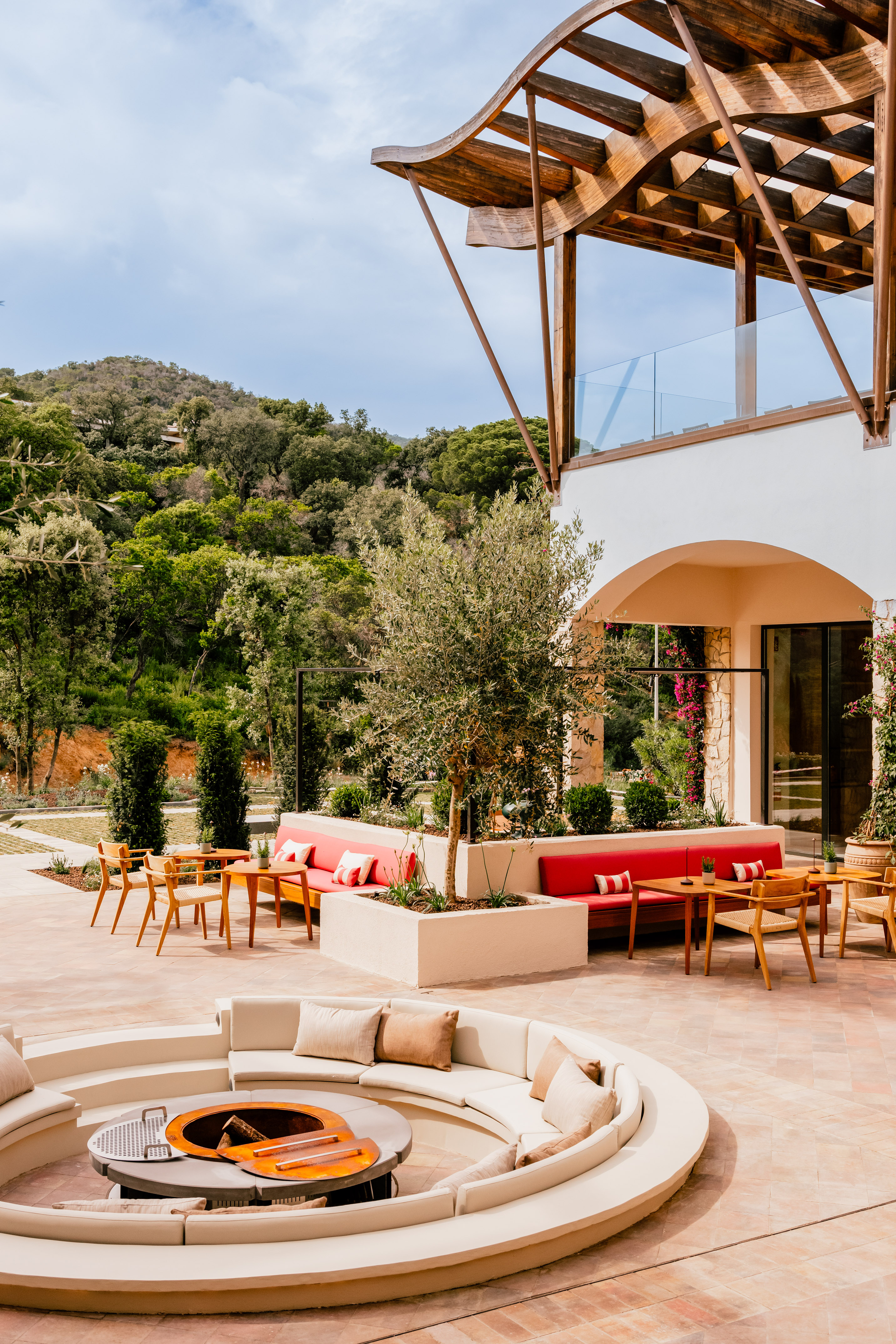 Modern outdoor patio with fire pit, red lounge seating, and lush mountain backdrop.