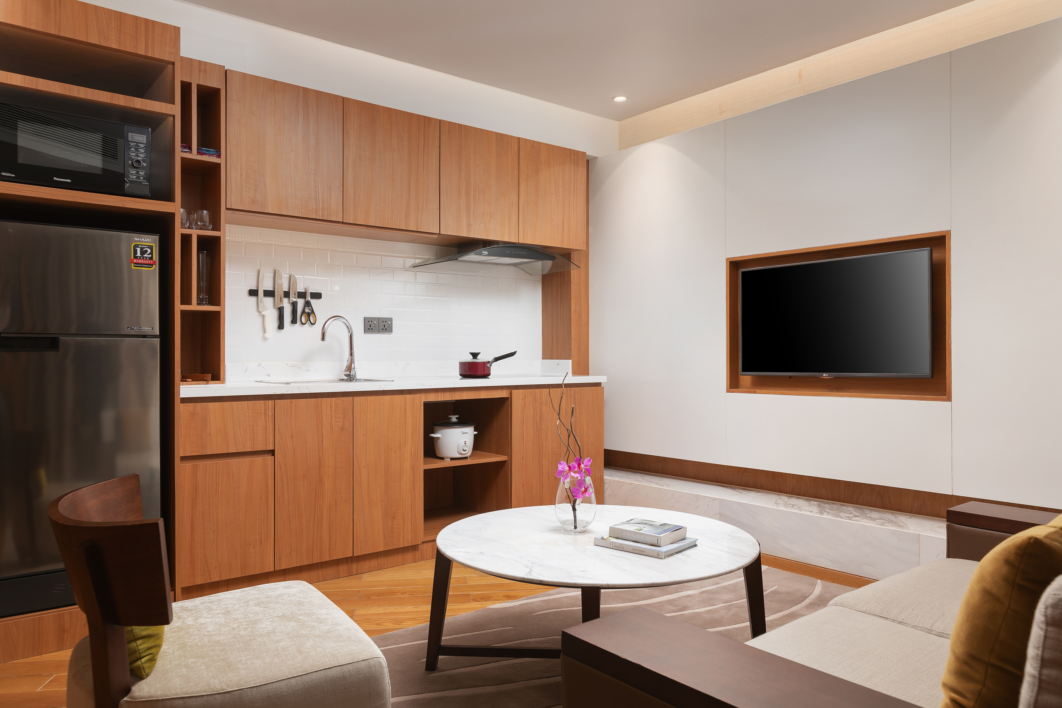 Compact hotel suite kitchenette, living area, smart TV, and wooden decor.