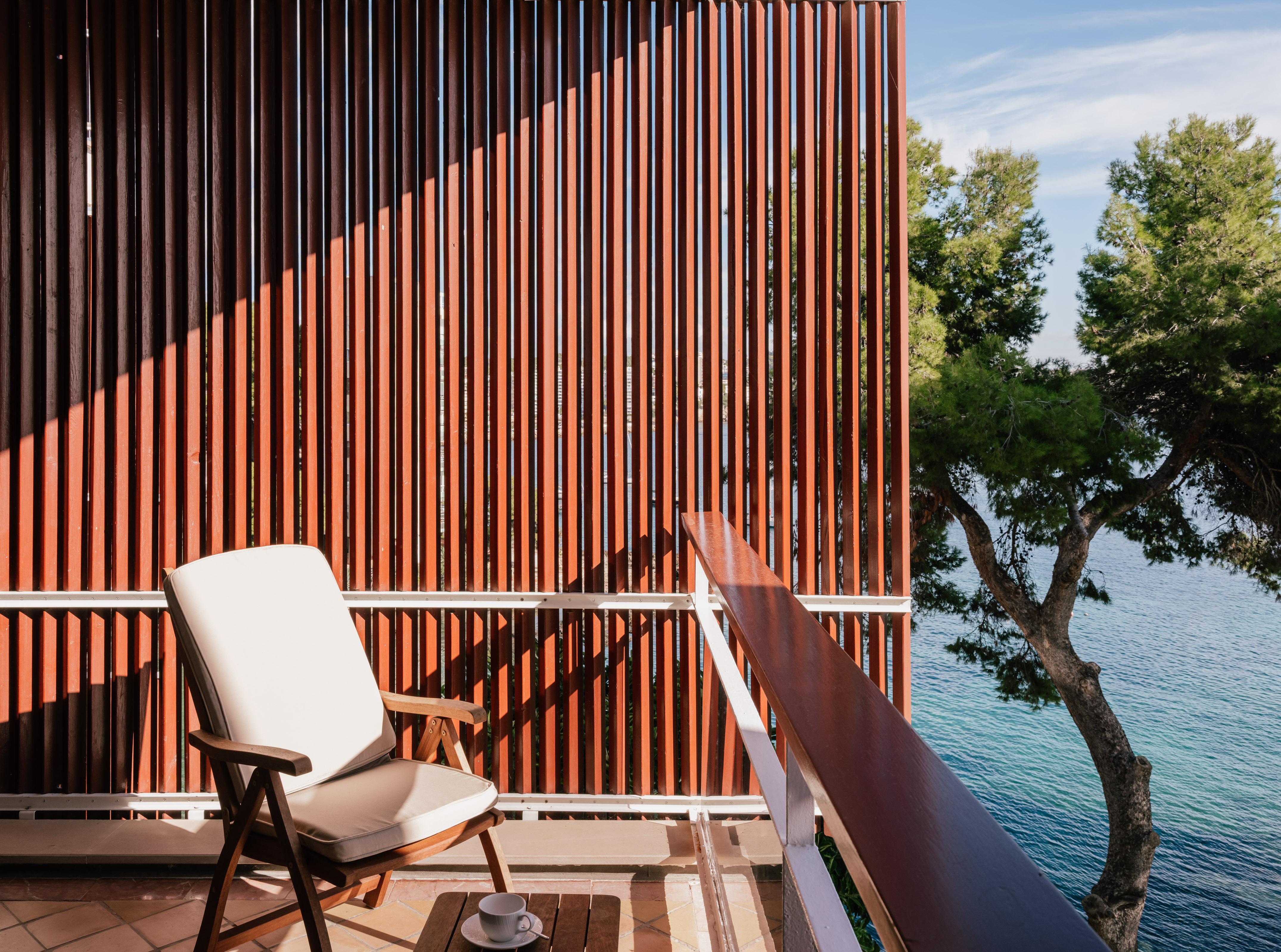 Sunny balcony with wooden privacy screen, outdoor chair, and ocean view.