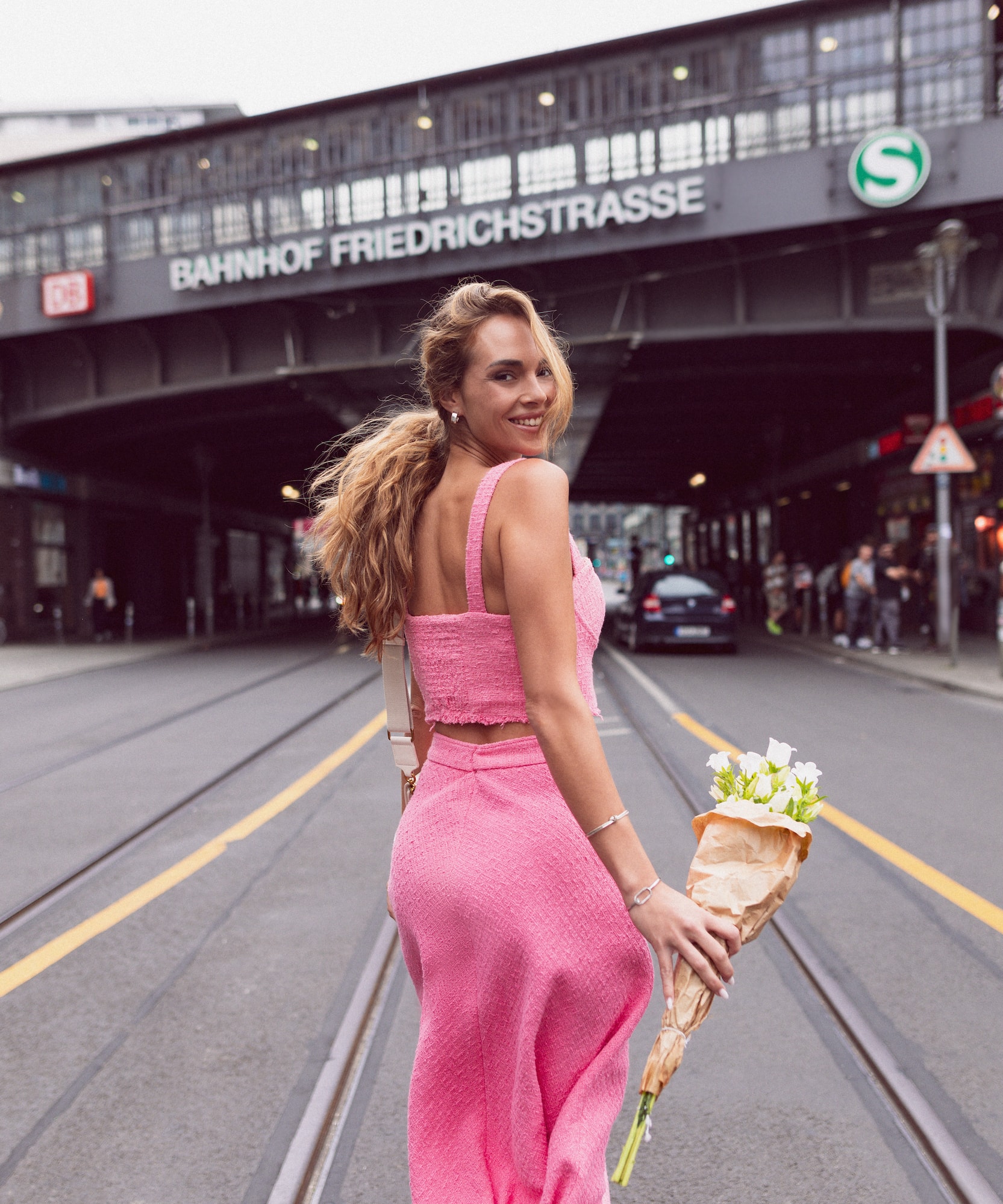 Woman in pink outfit holding flowers on Berlin street, Bahnhof Friedrichstrasse.
