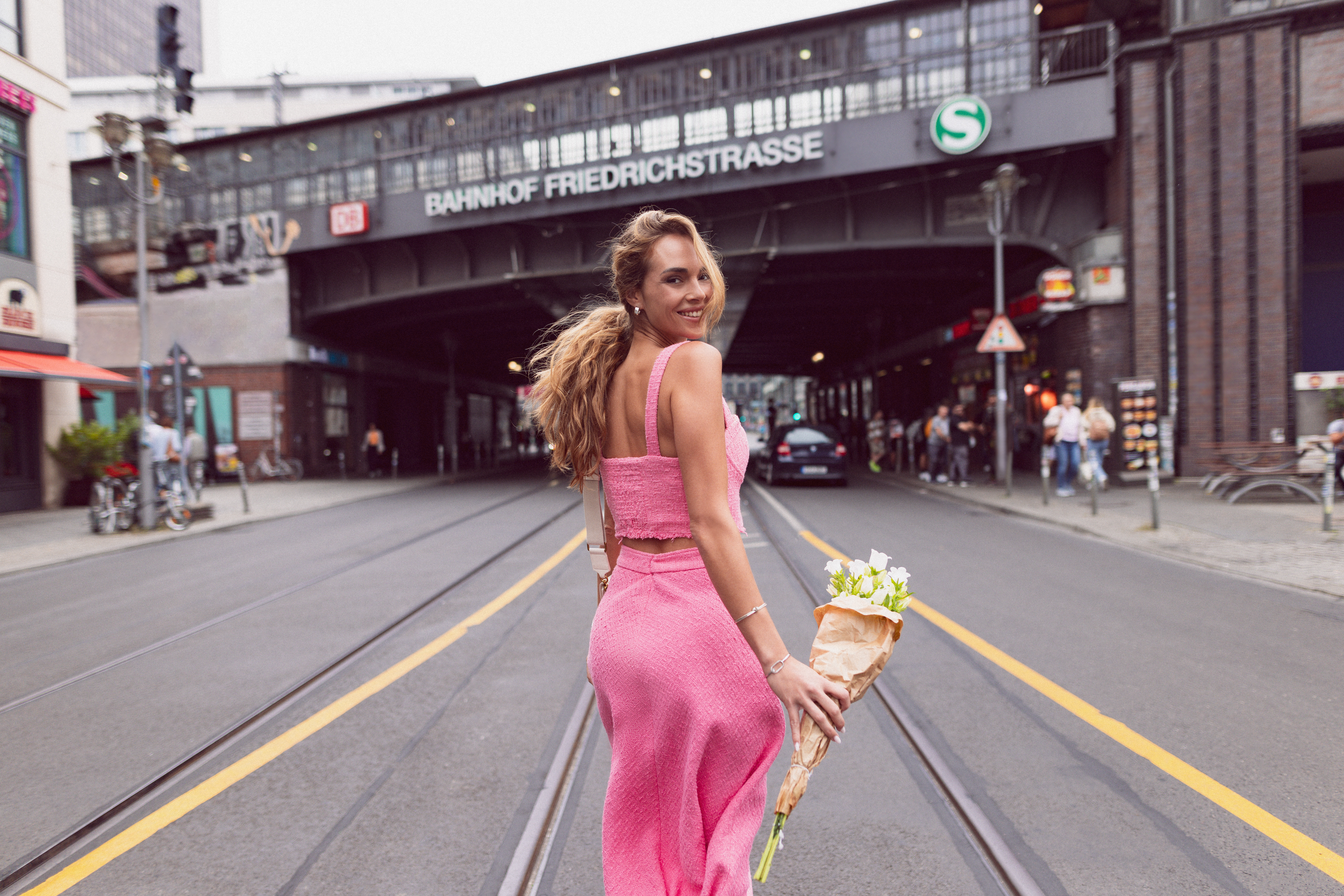 Woman in pink outfit holding flowers on Berlin street, Bahnhof Friedrichstrasse.