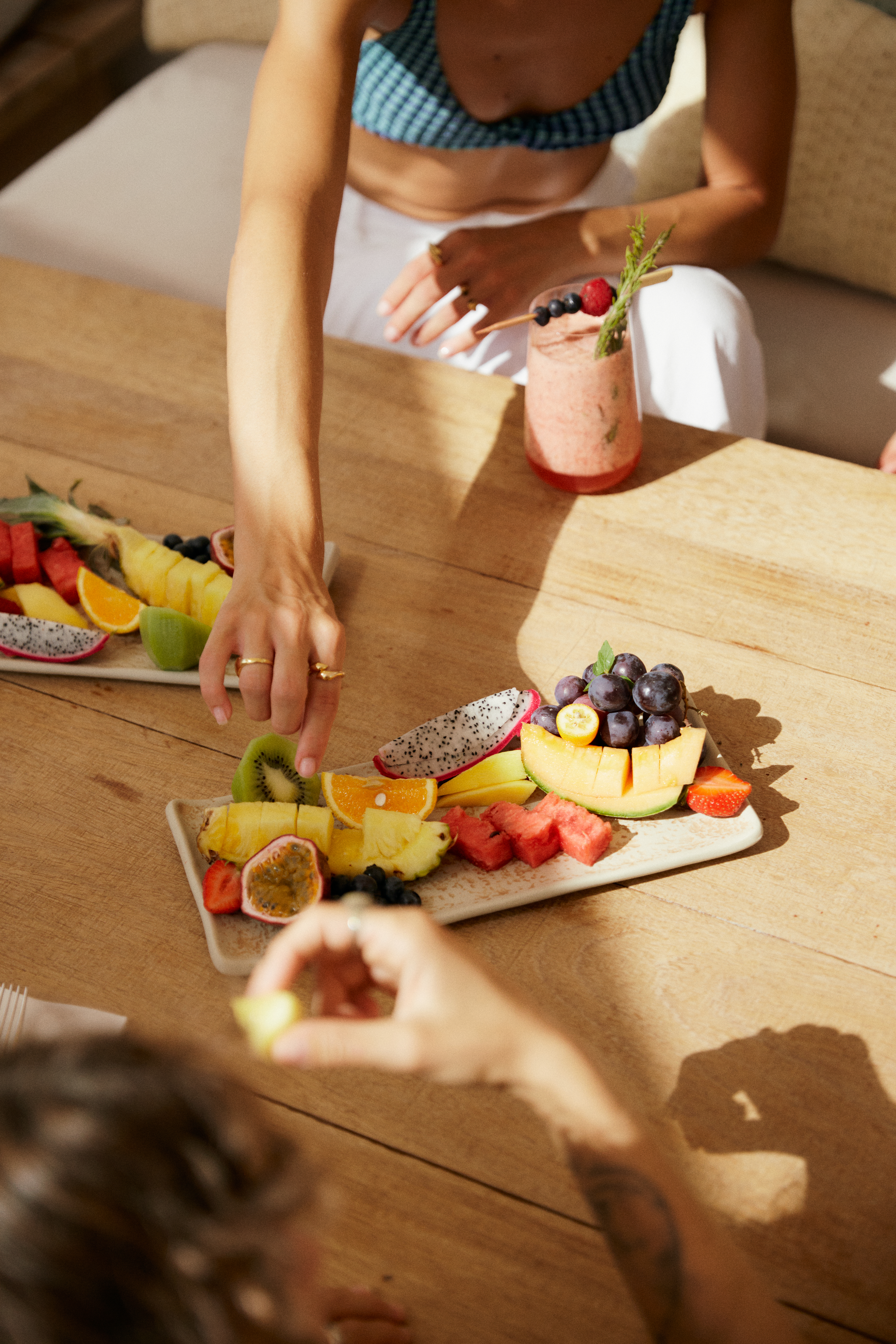 Colorful tropical fruit platters shared at a wooden table with a smoothie.