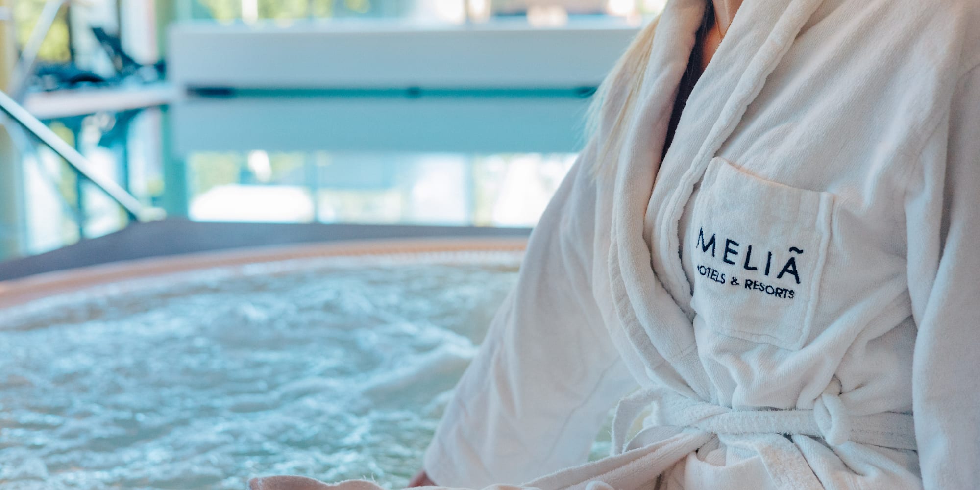Woman in Melia Hotels bathrobe by a bubbling spa jacuzzi.