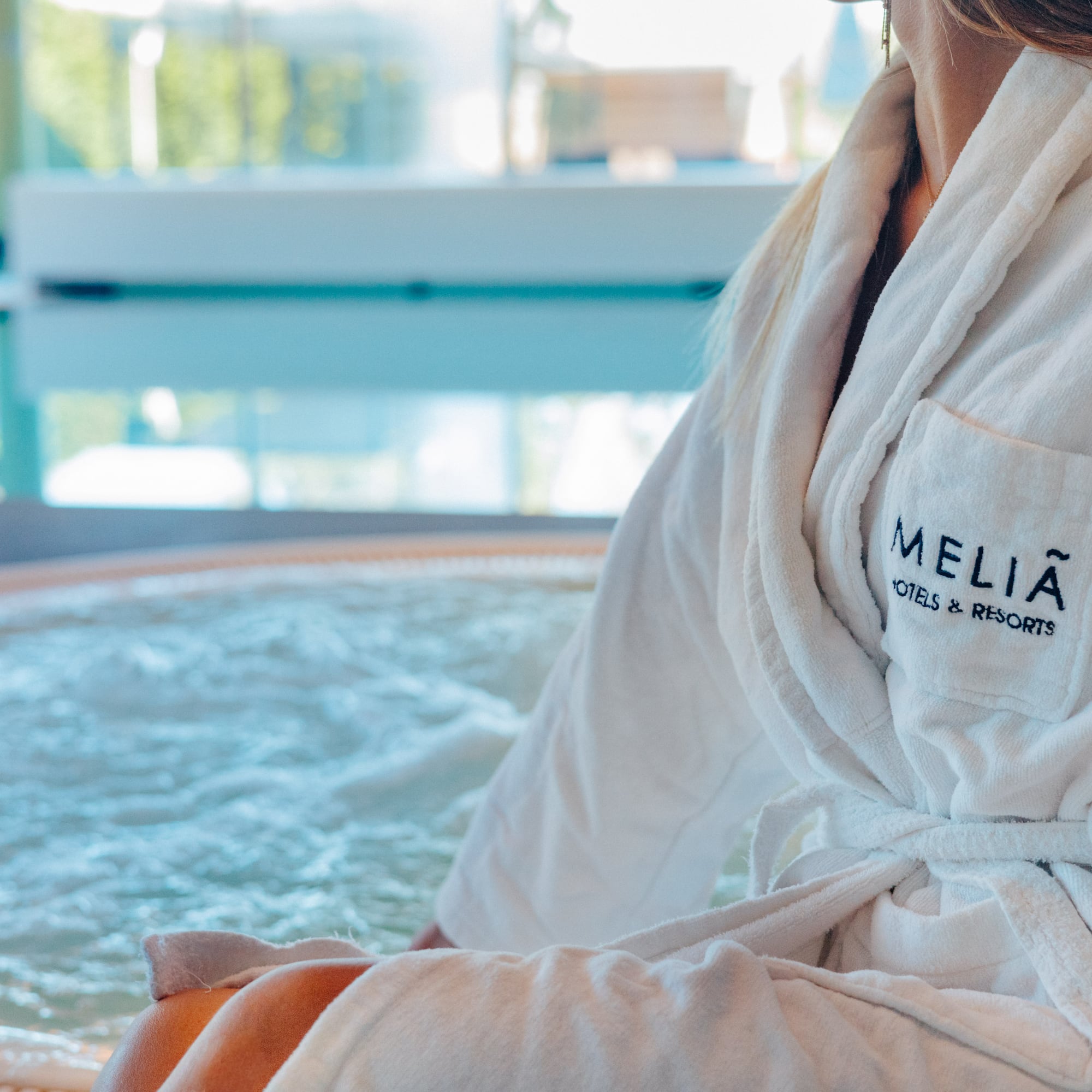Woman in Melia Hotels bathrobe by a bubbling spa jacuzzi.