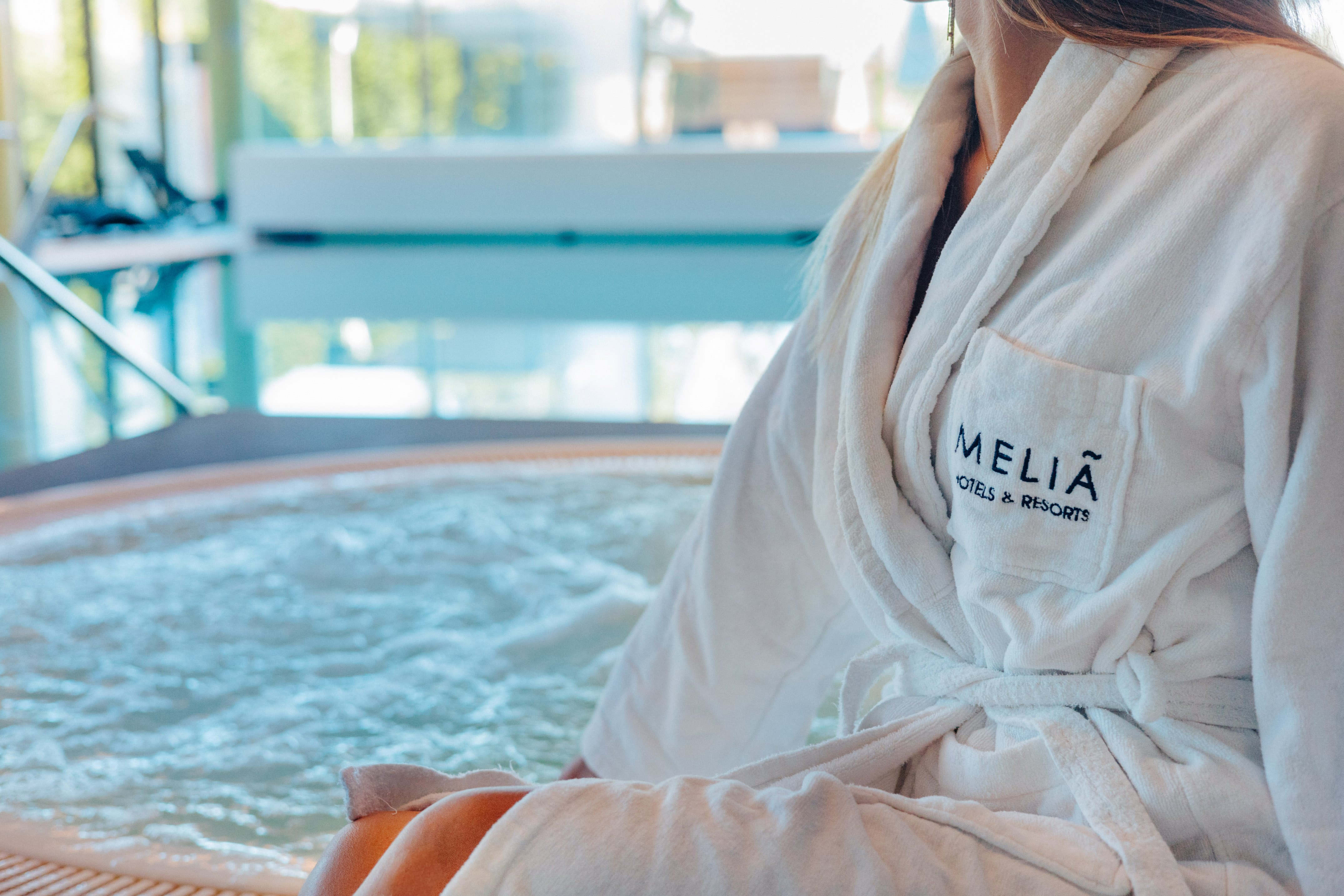 Woman in Melia Hotels bathrobe by a bubbling spa jacuzzi.