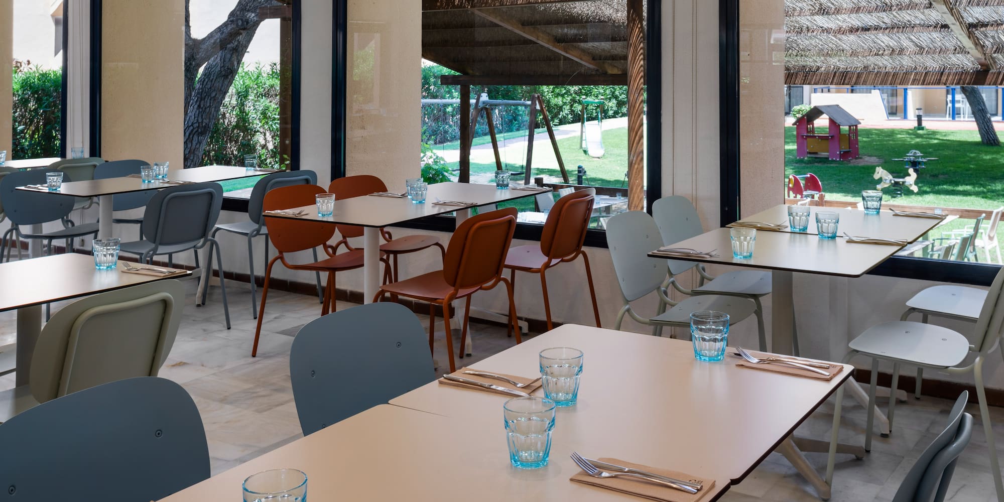 Restaurant tables set with cutlery, outdoor playground view, family dining area.