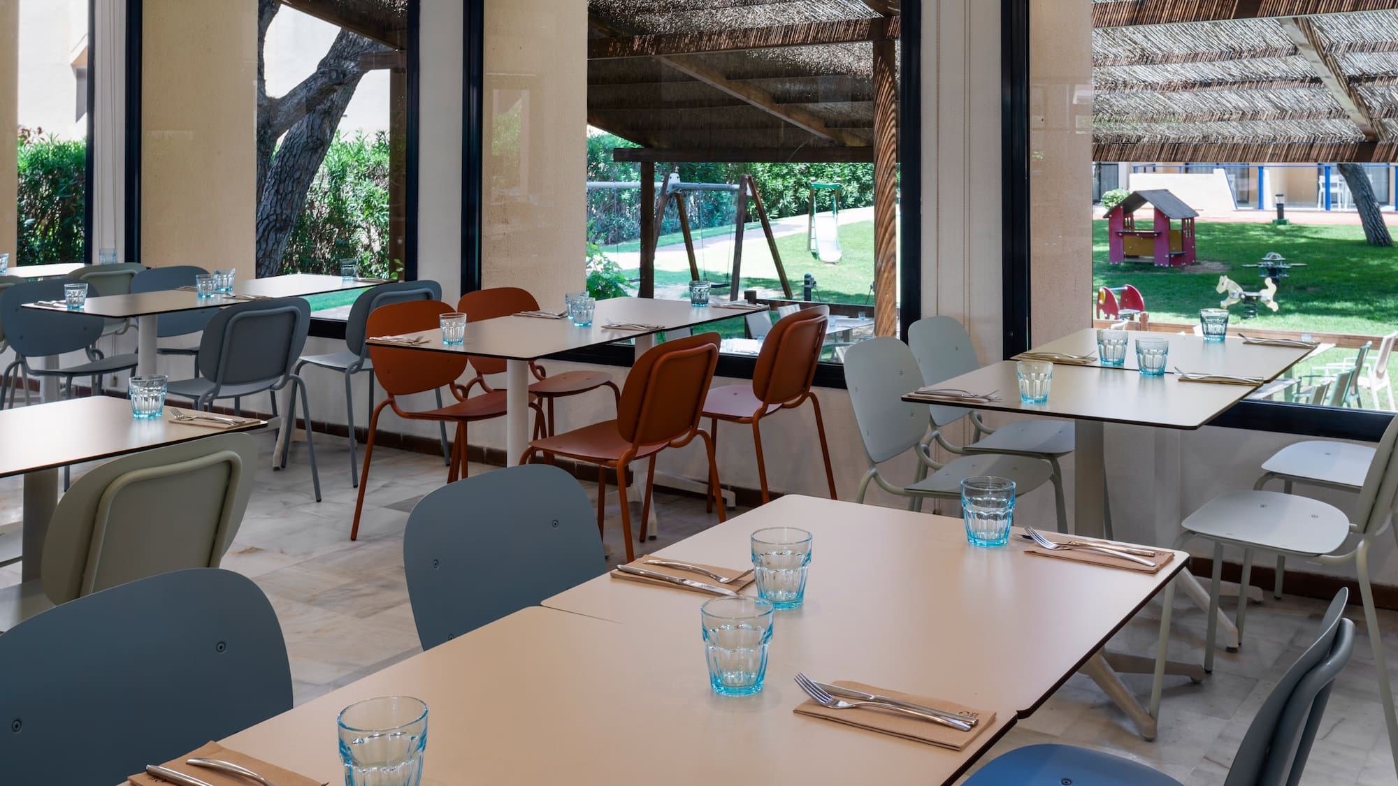 Restaurant tables set with cutlery, outdoor playground view, family dining area.