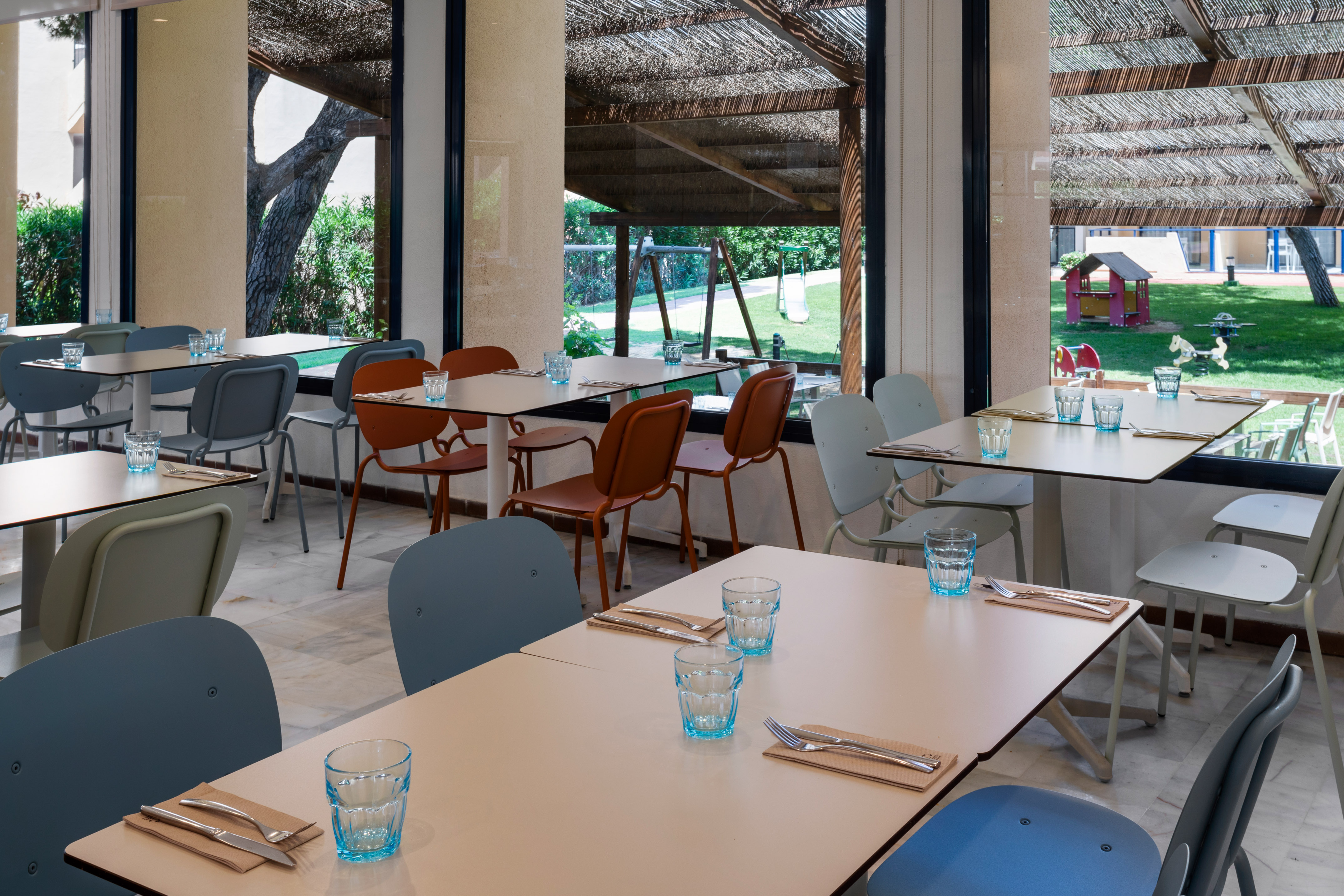 Restaurant tables set with cutlery, outdoor playground view, family dining area.