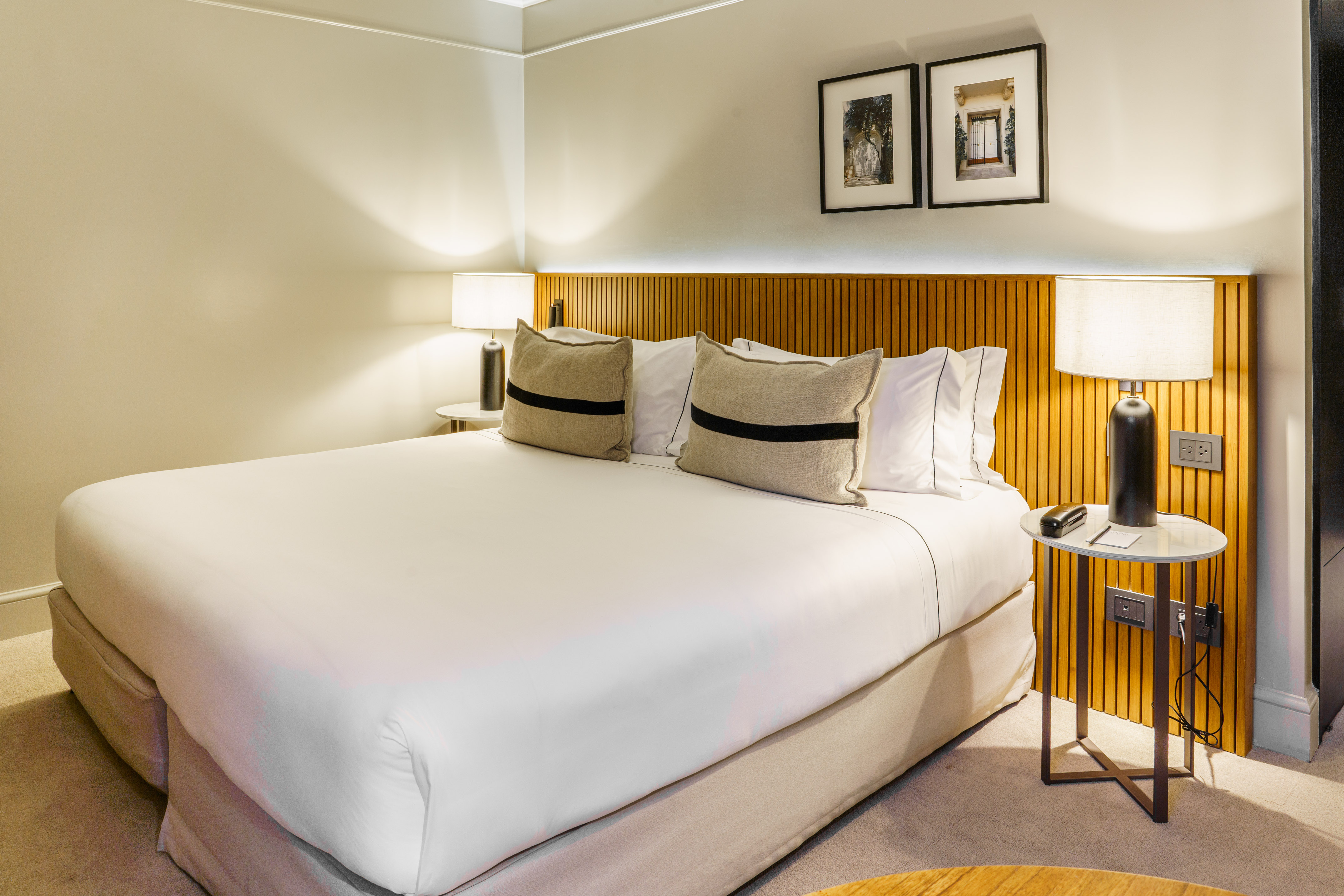 Luxury hotel room with queen bed, wooden slatted headboard, and modern lamps.
