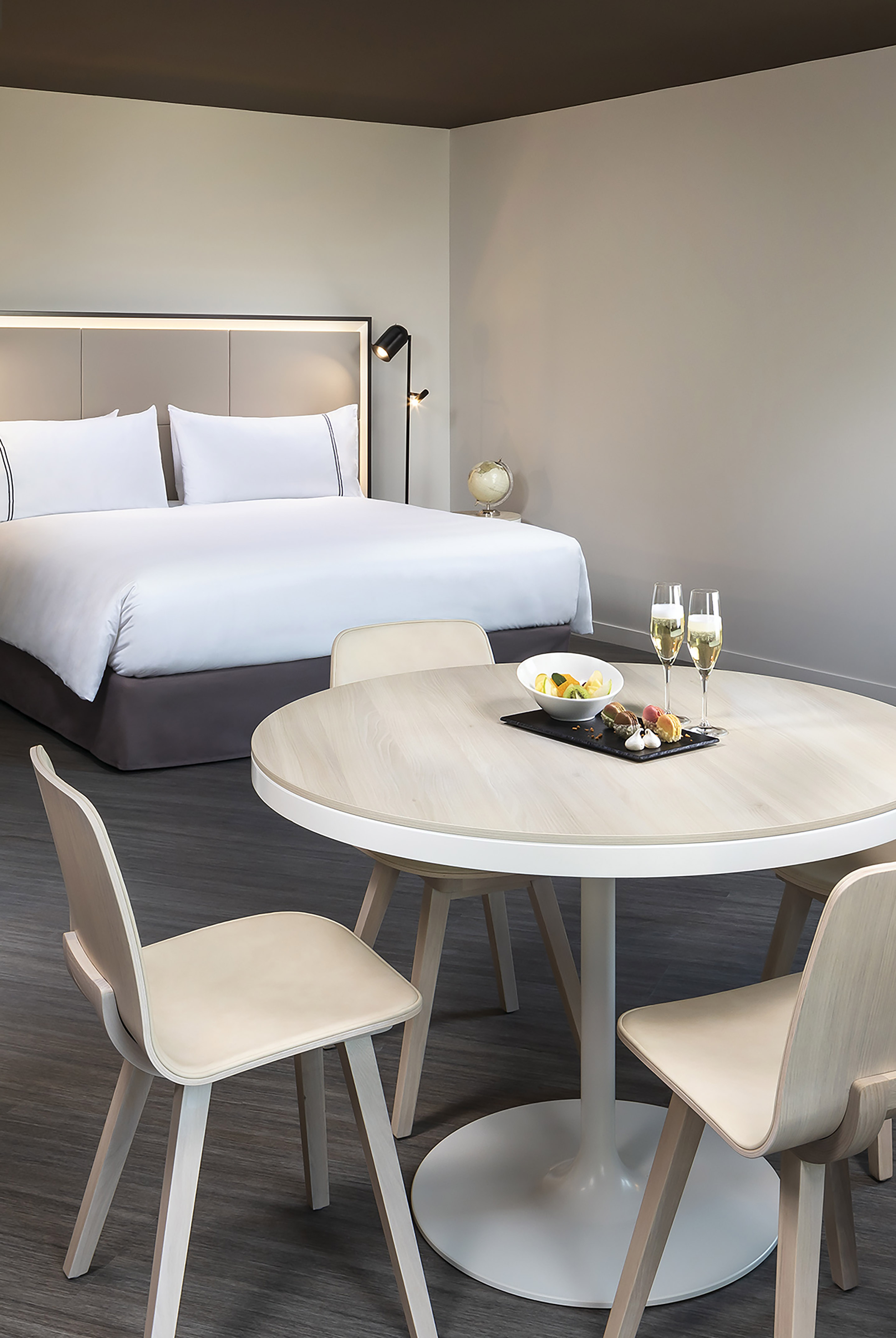Luxury hotel suite with modern bed, dining table, fruit, and champagne.